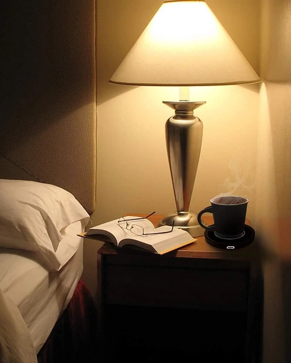 a lamp and a book on a table with a cup of coffee warmed by a smart coffee warmer