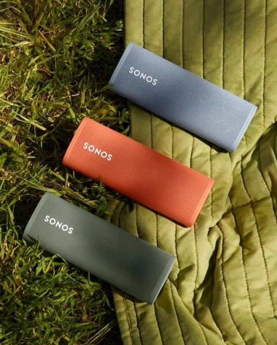 a trio of sonos roam speakers laying on the grassy floor and blanket