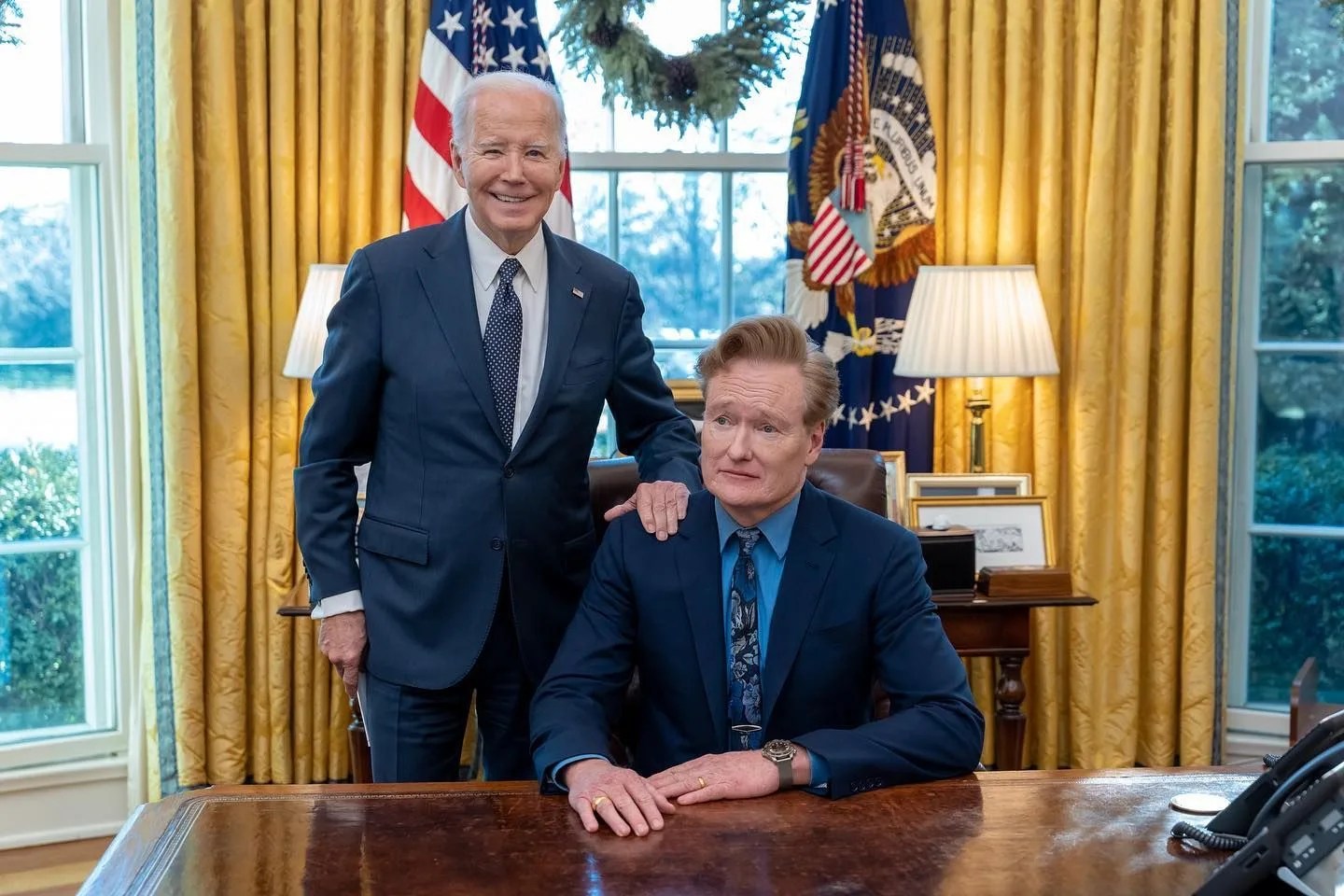 a man standing next to a man sitting at a table