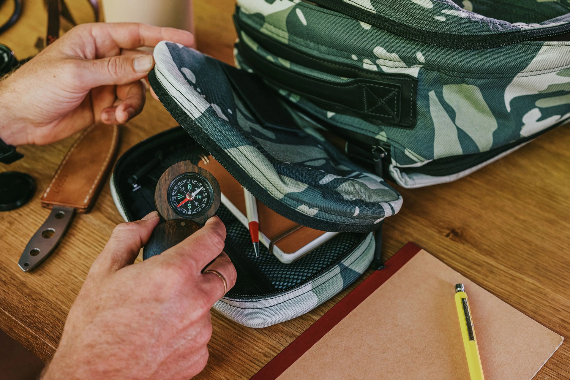 man packing watch and tools away in camo pouch beside goruck bag