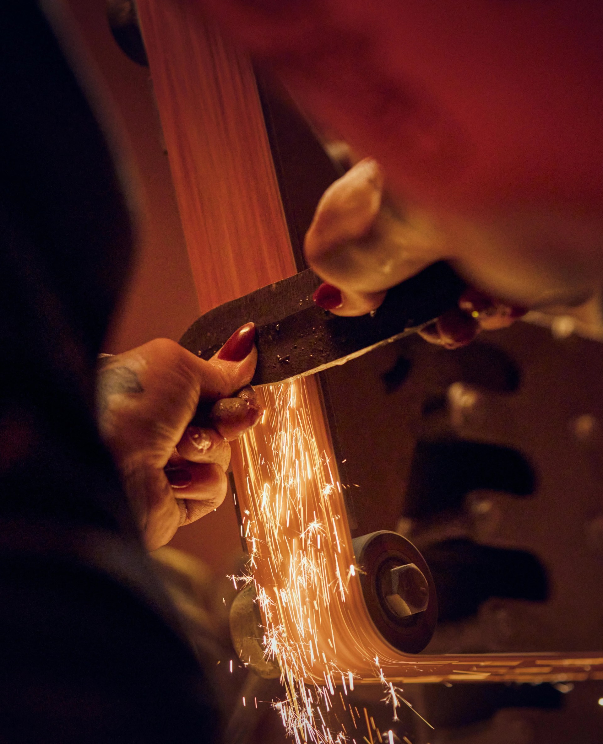 a person making a knife blade on a machine with sparks flying