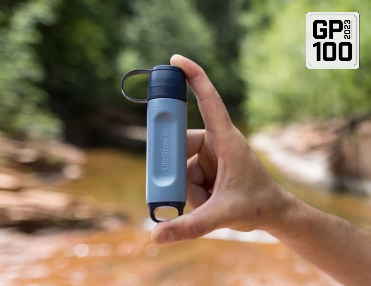a hand holding a lifestraw by a river