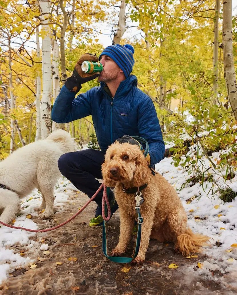 a person drinking a can of sierra nevada beer crouched by a dog