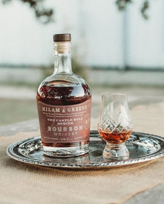 a bottle of milam and greene whiskey and a glass of whiskey on a table