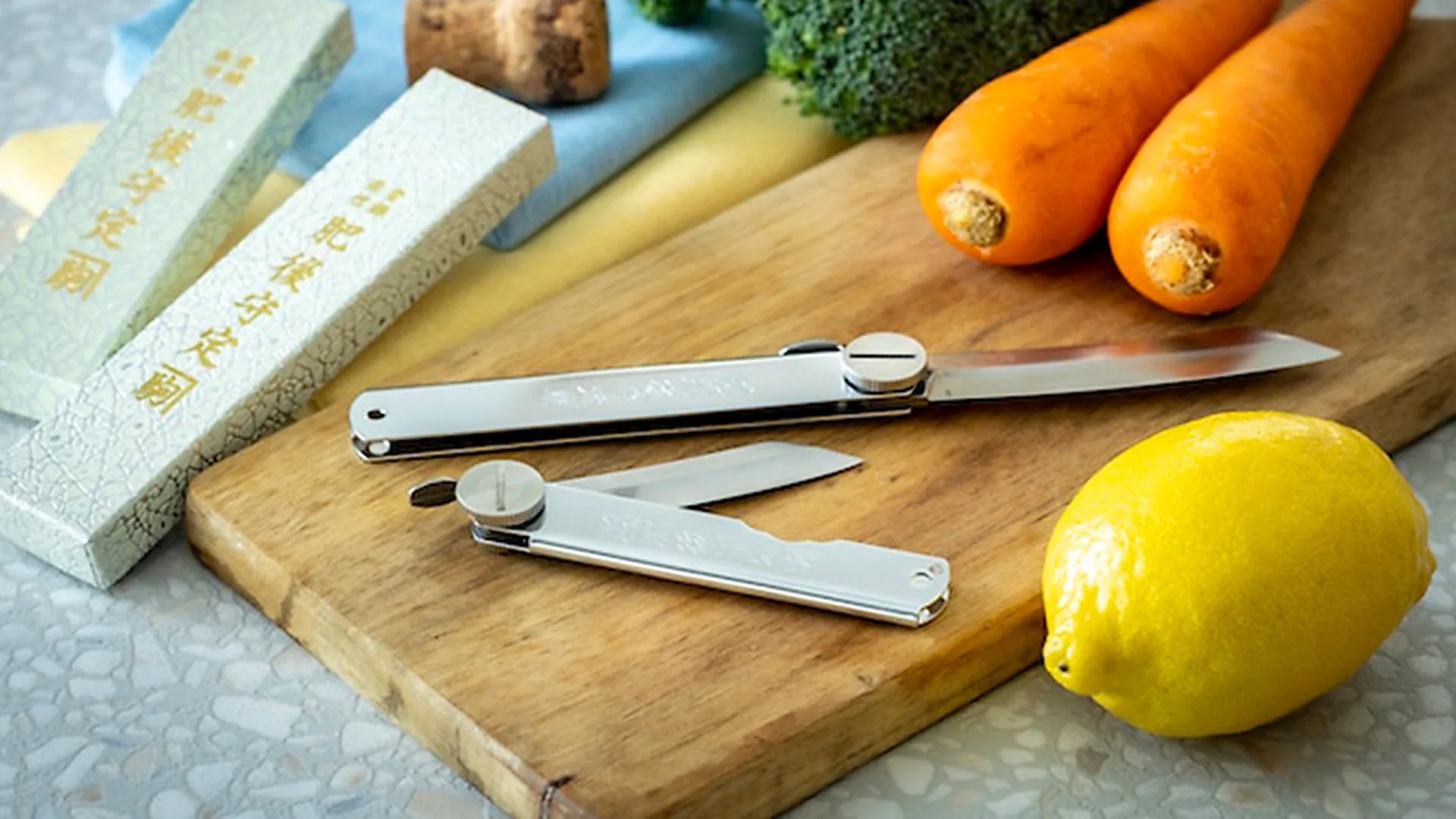 2 Screw Hinged Large Sized Higonokami Knives on a cutting board with carrots and a lemon