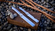 two Screw Hinged Large Sized Higonokami Knives on a block of wood next to sticks and stones