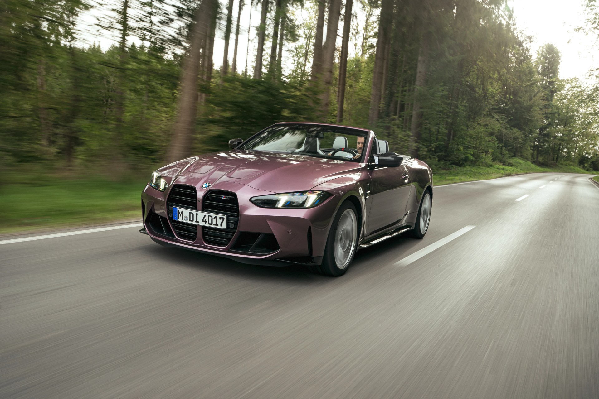 ruby colored bmw m4 convertible driving towards you on a forest road