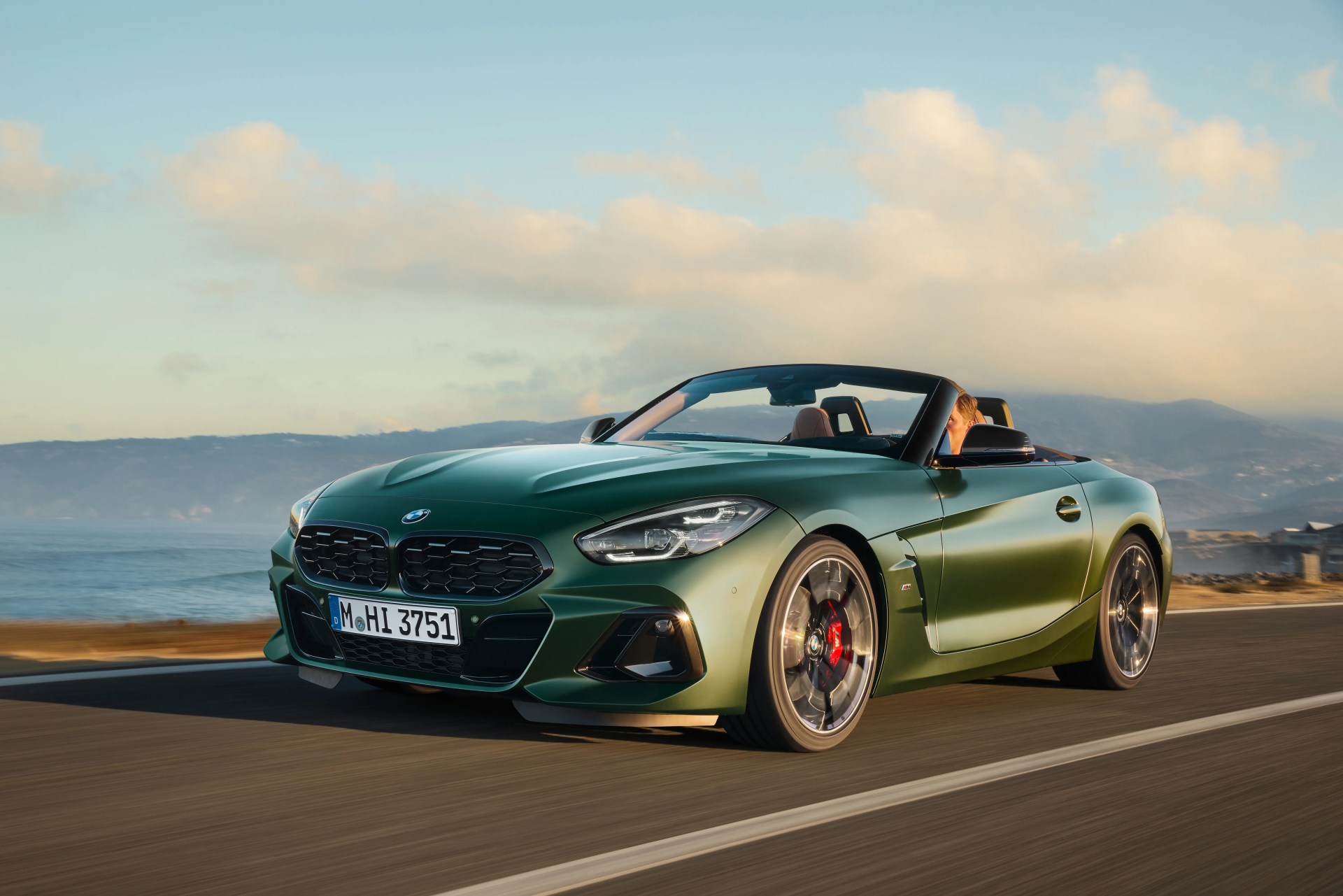 a green bmw convertible driving along the coast at sunset