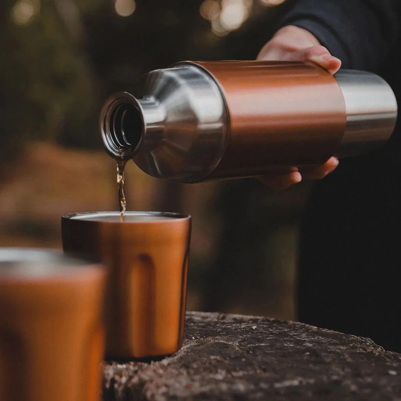 a person pouring a liquid into a glass from a high camp firelight flask 750
