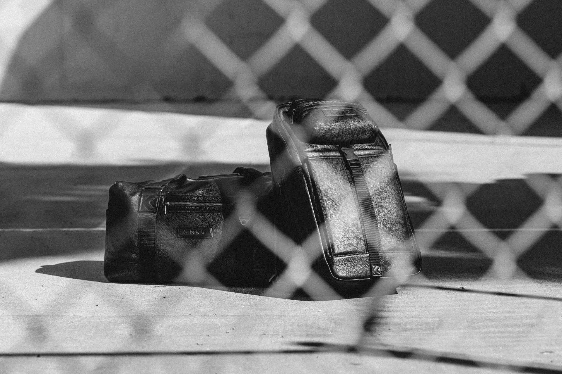 a black and white image looking through a fence of two bags sitting on the ground