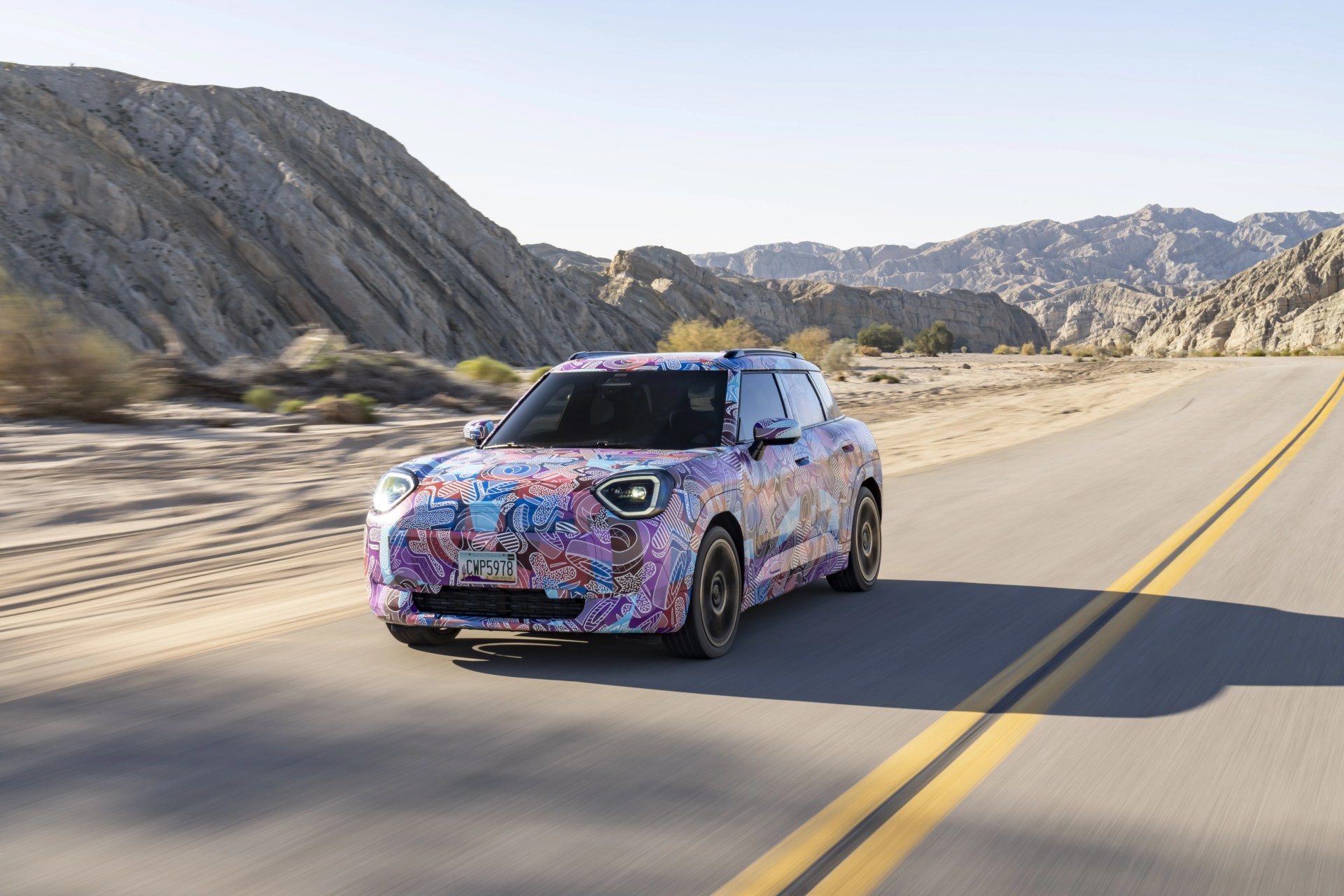 camouflaged mini aceman crossover driving towards you on a two lane road
