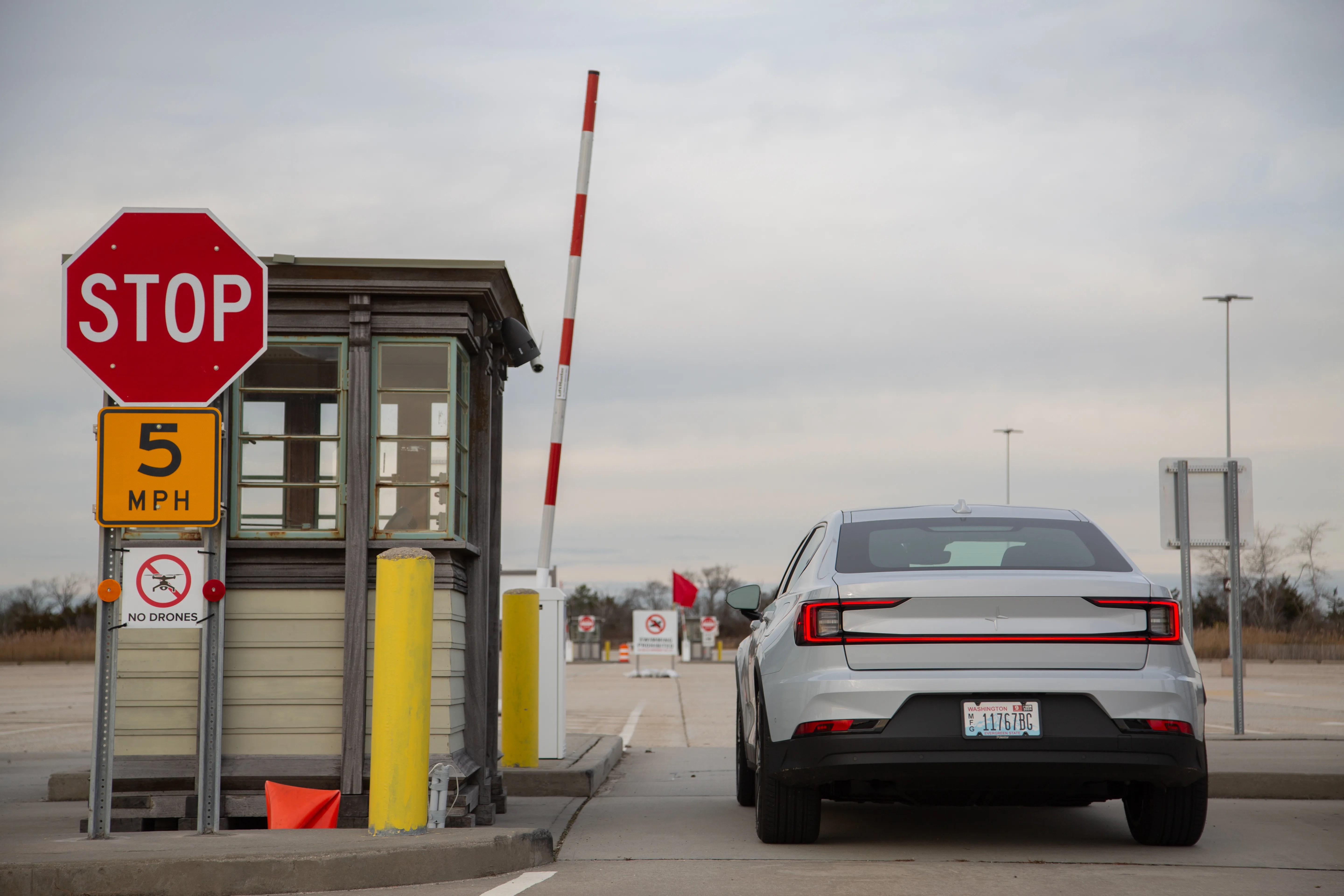A white sedan seen from the rear while stopped at an empty toll booth with the gate raised.