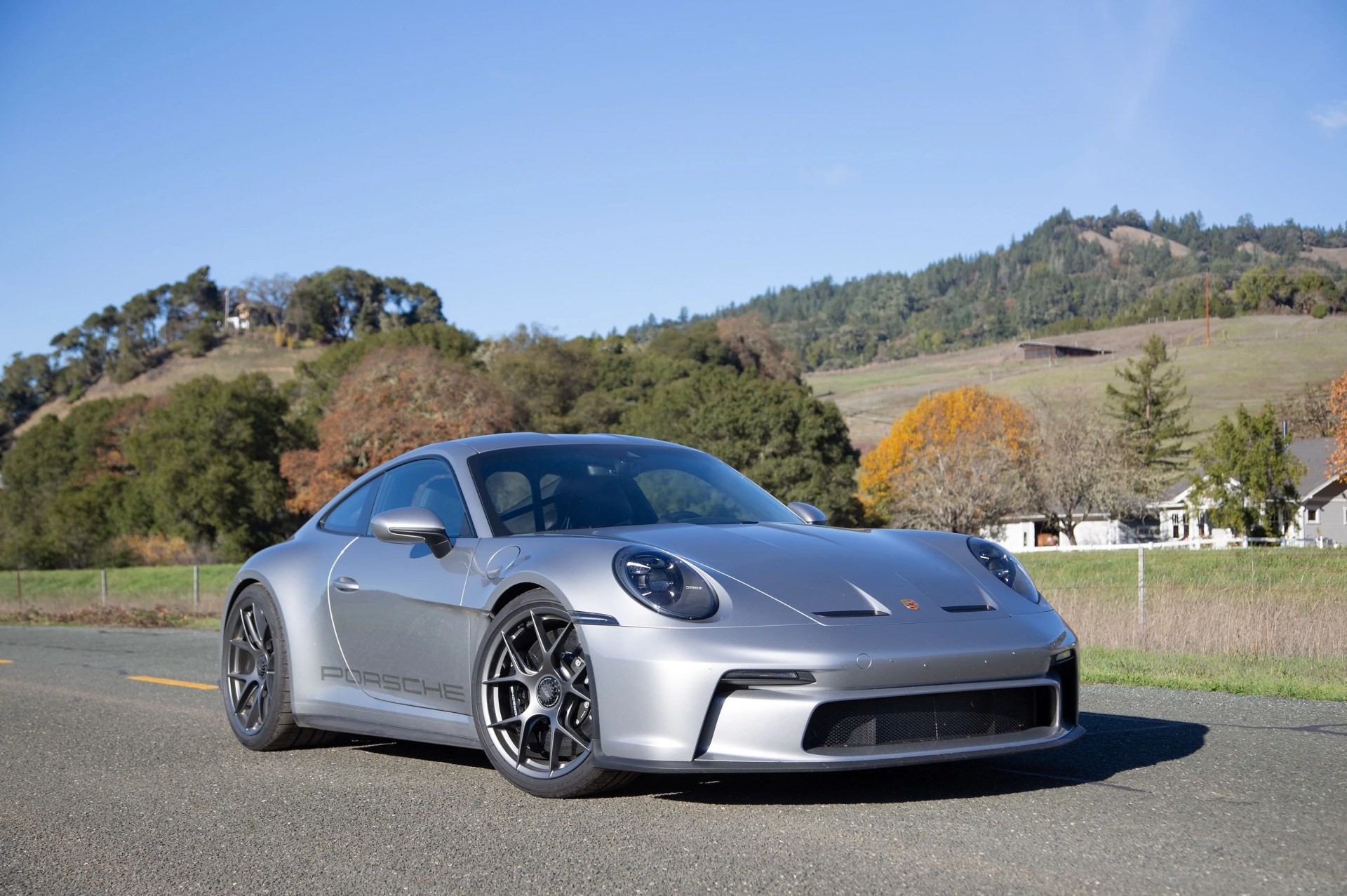 a silver sports car parked on a road with trees and hills in the background