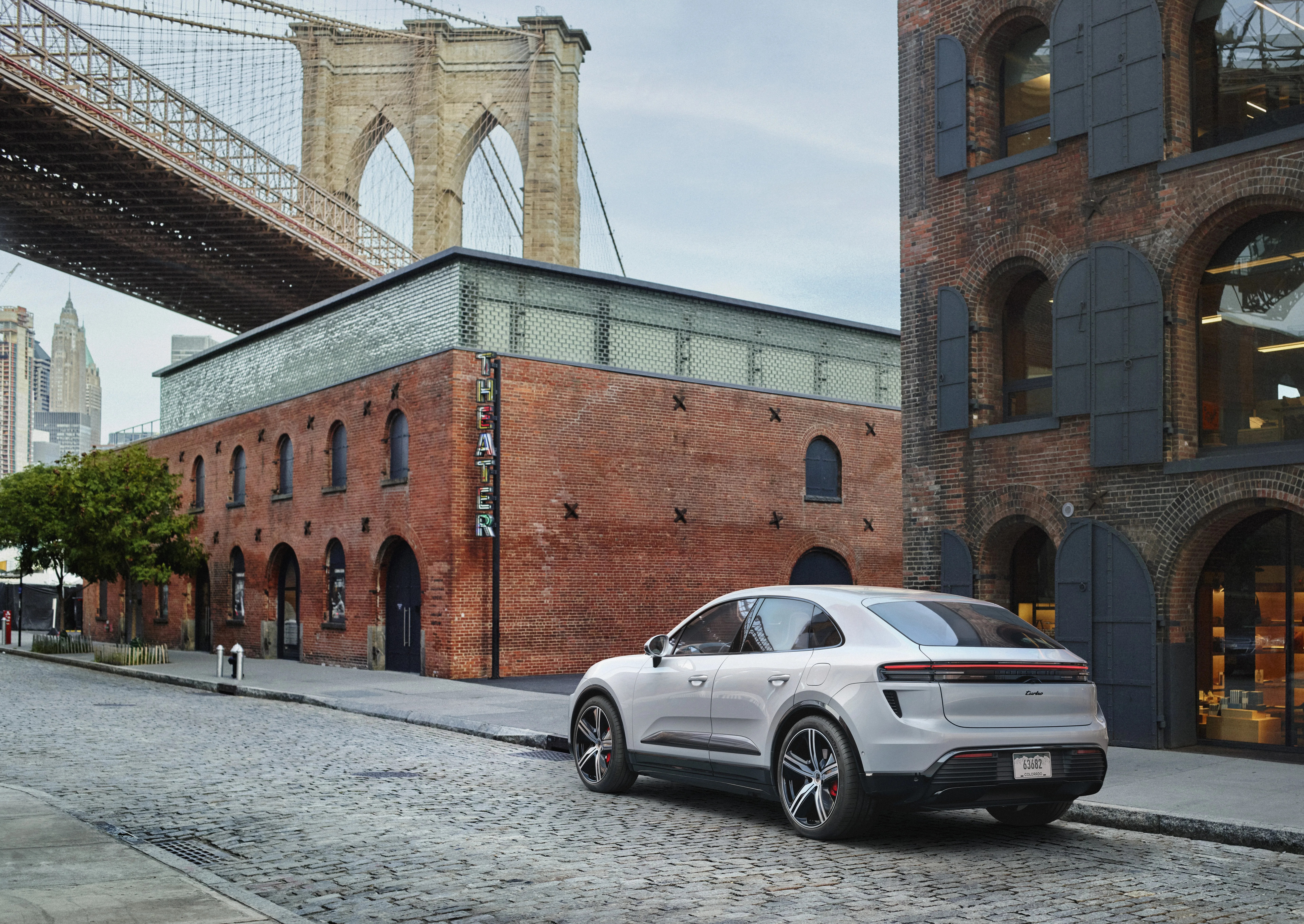 the rear view of the 2024 porsche macan turbo electric parked in downtown brooklyn on a cobblestone street with the brooklyn bridge in the background