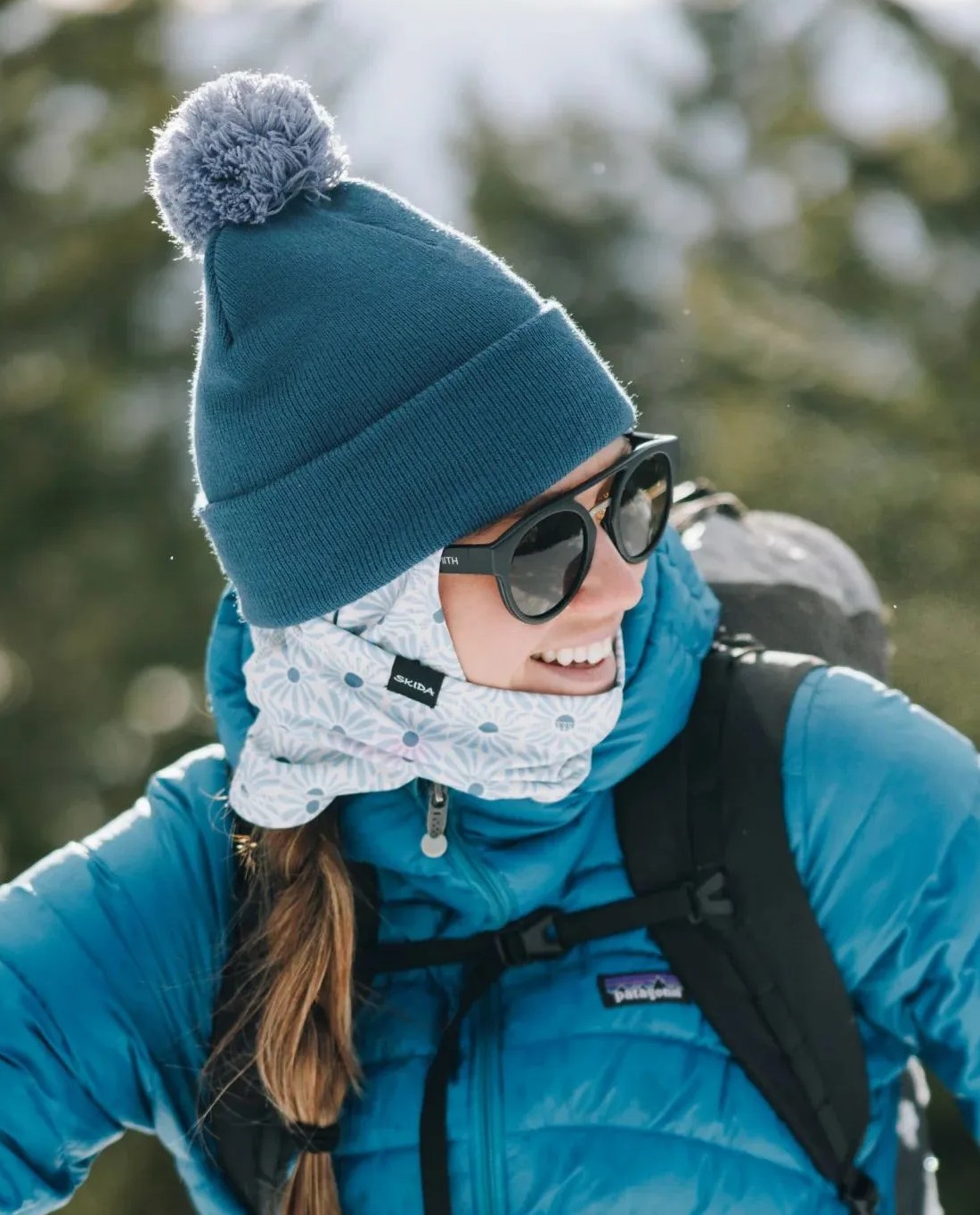 a person wearing a blue coat and sunglasses with a backpack and a skida shimmer balaclava