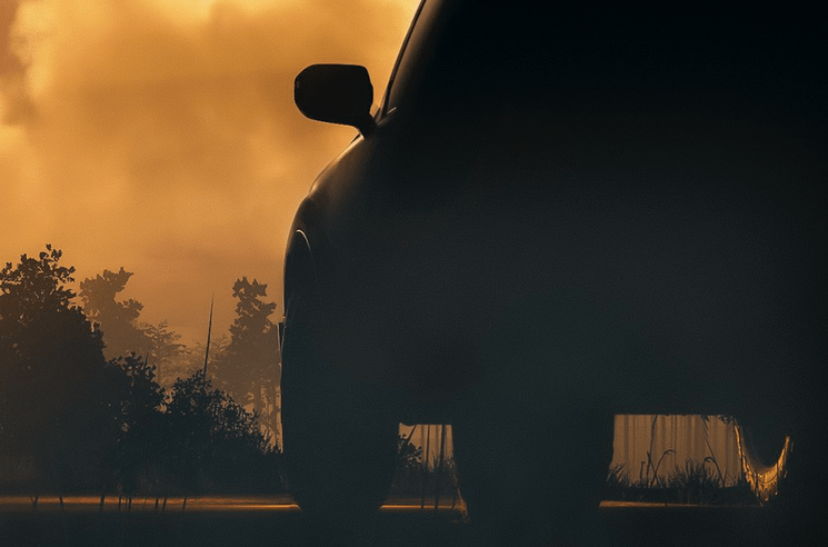 a car driving on a road with trees and a fire in the background