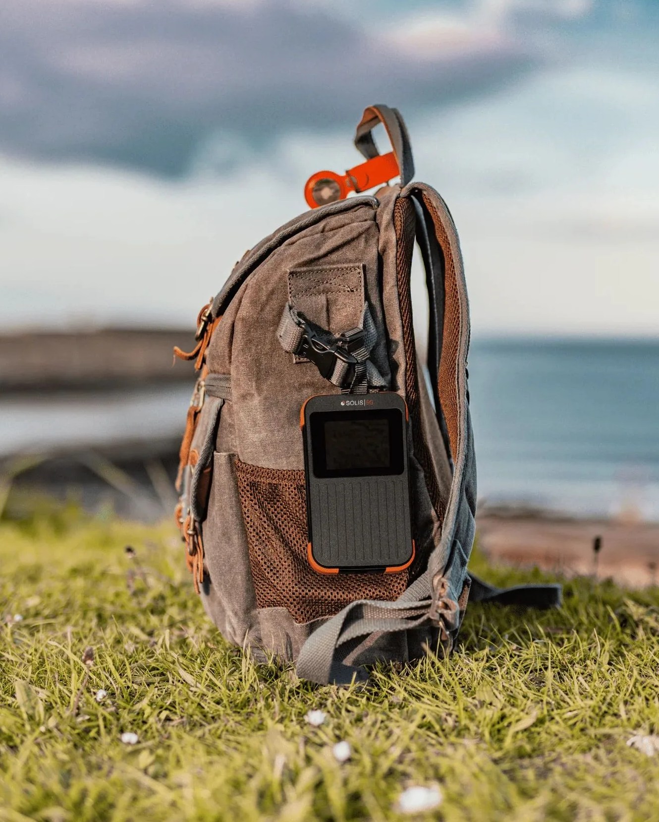 a backpack on grass by the water with solis 5g hotspot and power bank