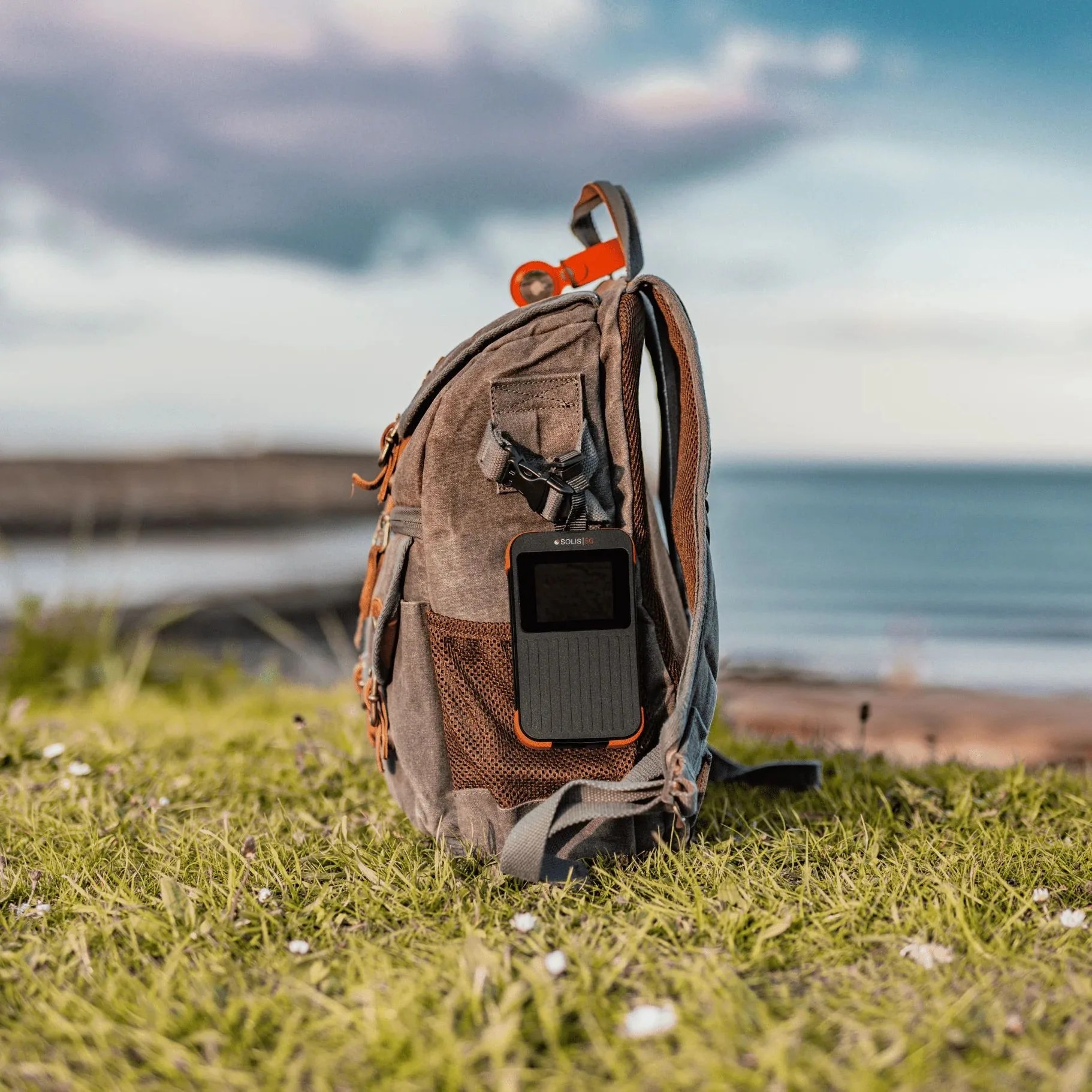 a backpack on grass by the water with solis 5g hotspot and power bank