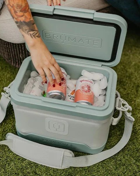 a person putting a drink into a magpack 12 can shoulder sling soft cooler