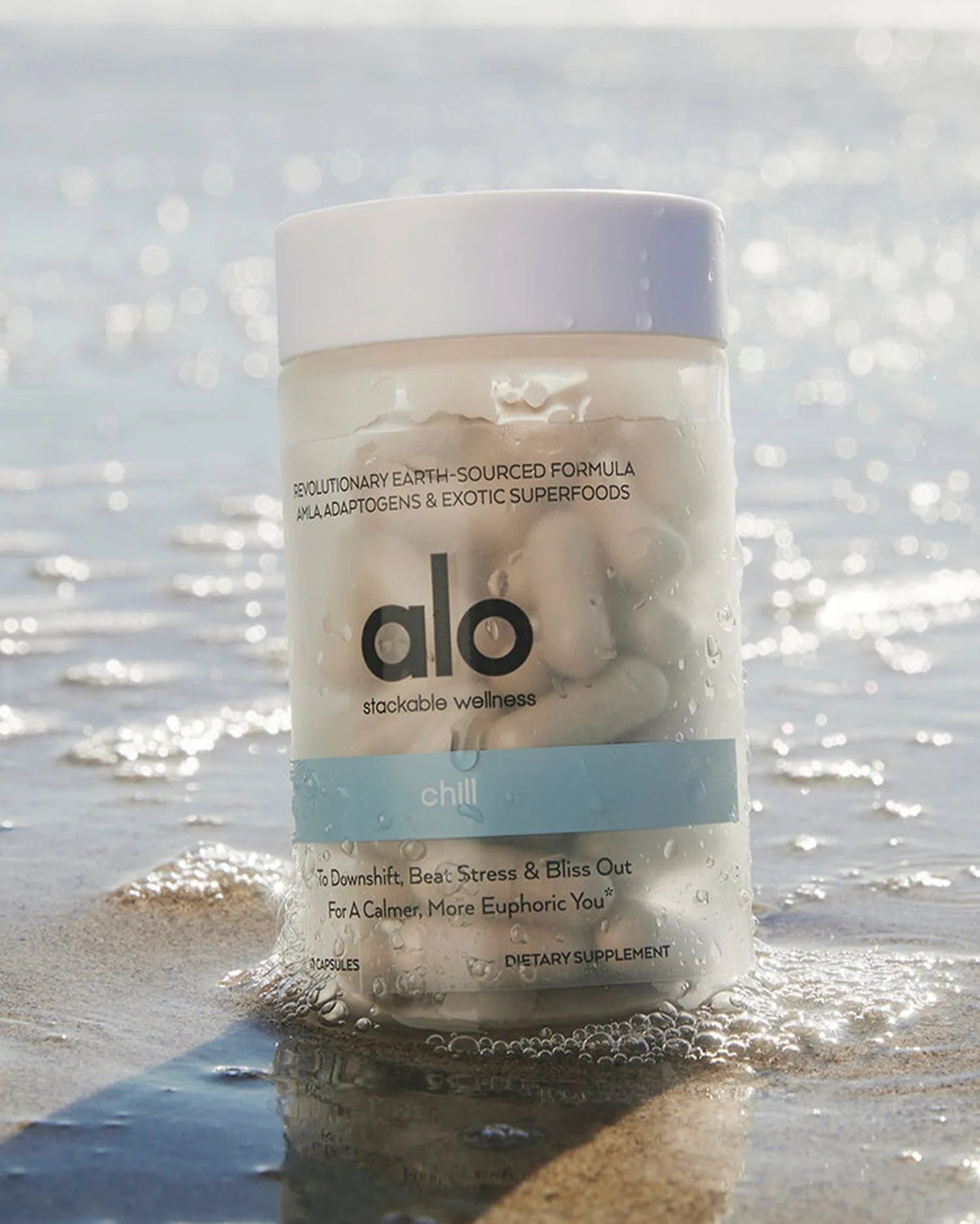 a bottle of capsules sitting in sand by the water