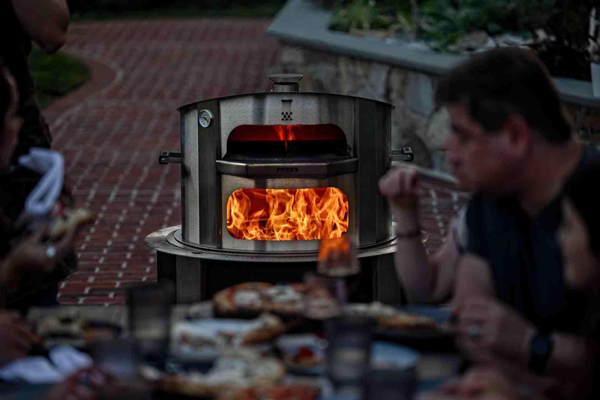 breeo live fire pizza oven in use, friends eating pizza