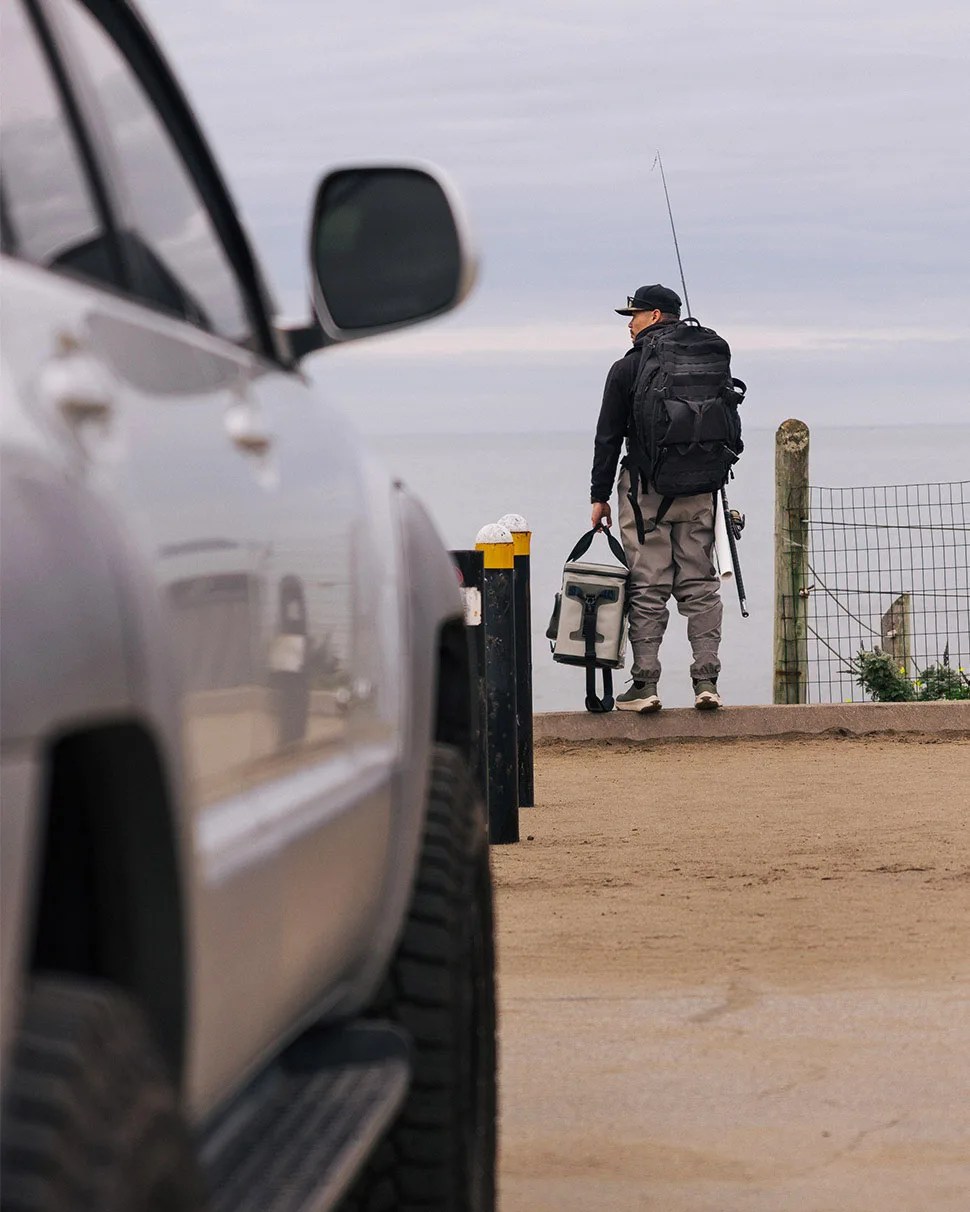 Daniel He looking off into the distance holding fishing gear wearing HOKA sneakers