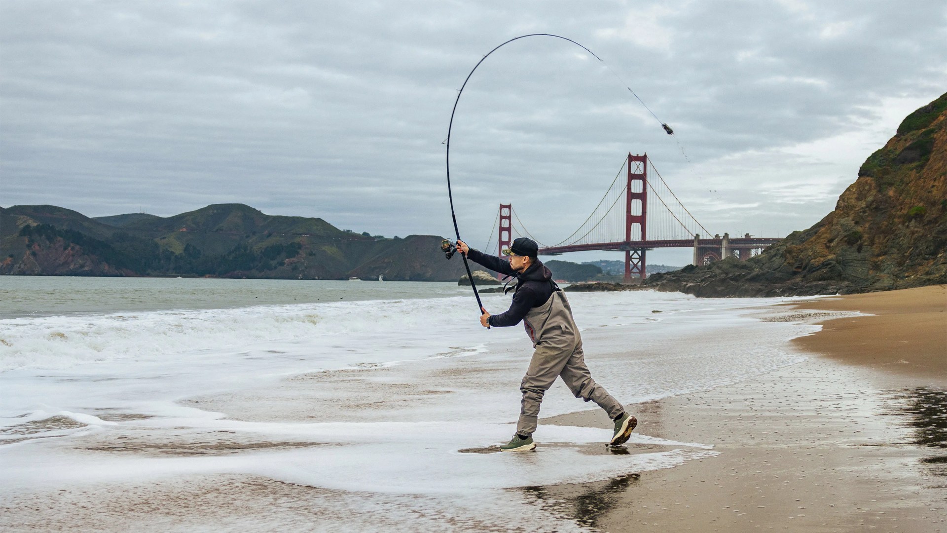 Daniel He fishing at the beach with the San Francisco bridge behind him