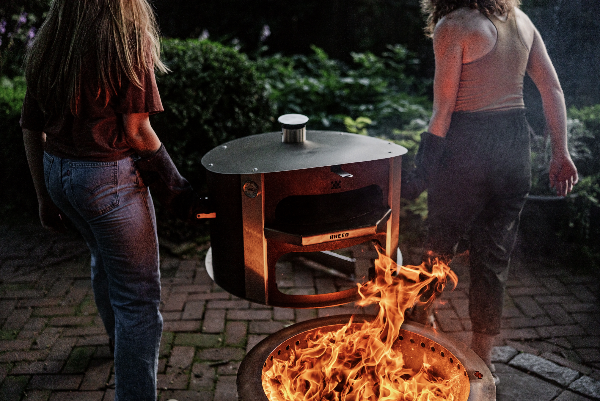 breeo live fire pizza oven being carried by two women