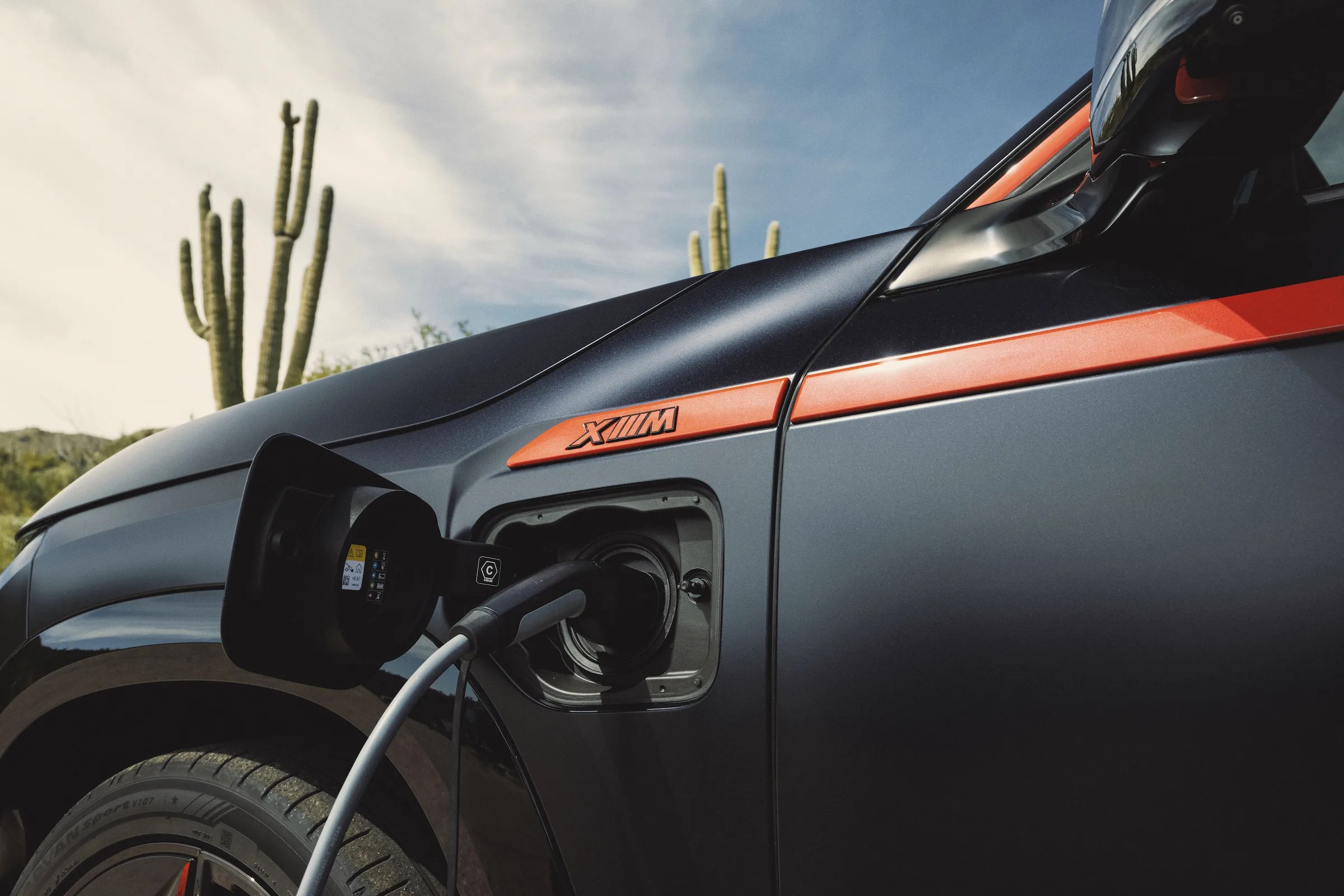 a red and black BMW xm plug in hybrid charging on a power cable in front of a cactus