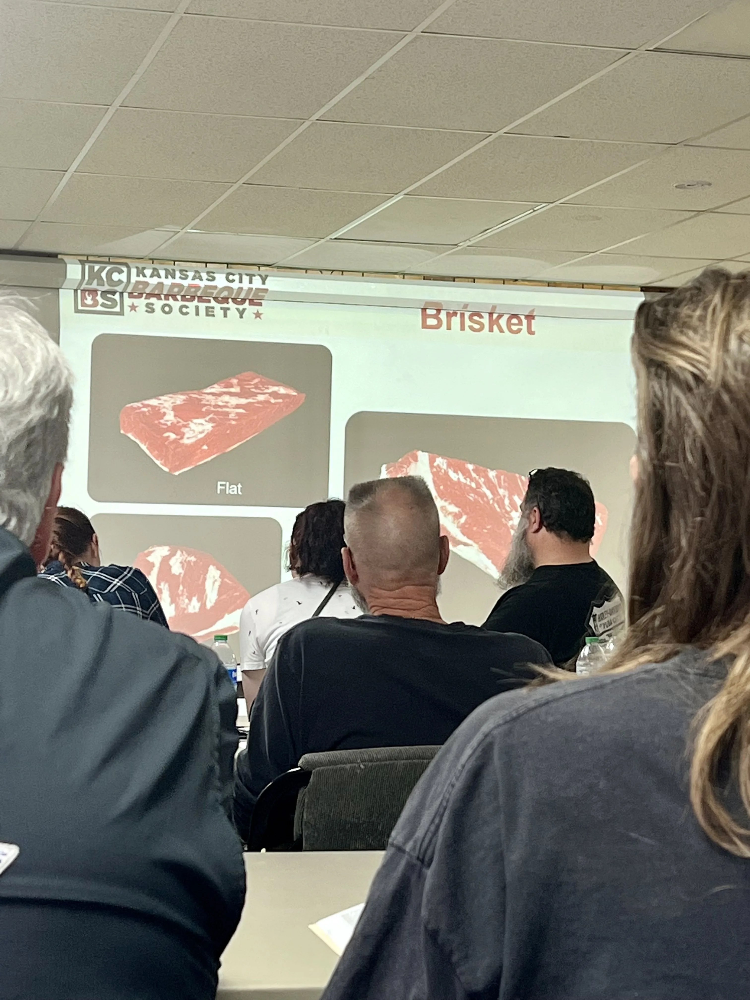 adults sit in a room looking at powerpoint presentation about meat