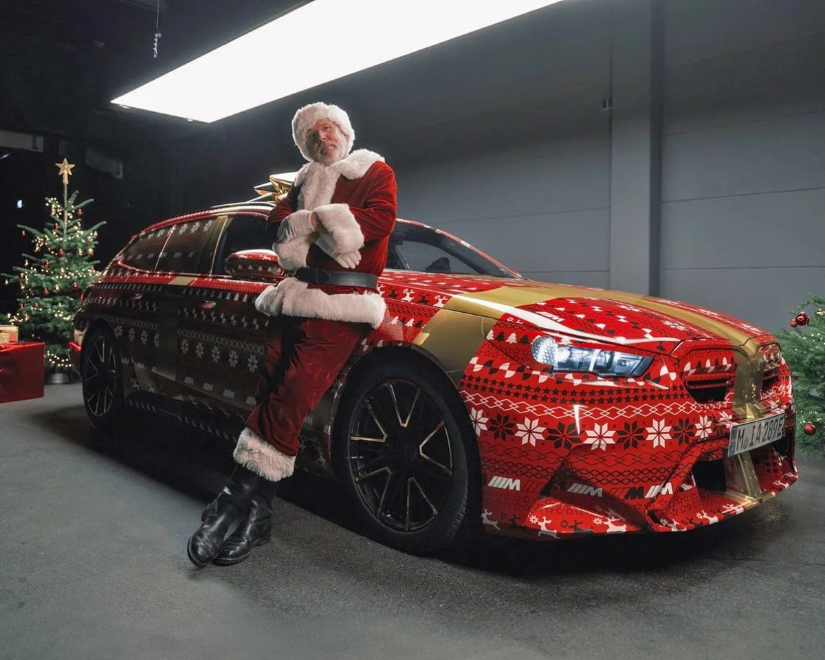 santa claus leaning against a bmw m5 station wagon wrapped like a christmas present