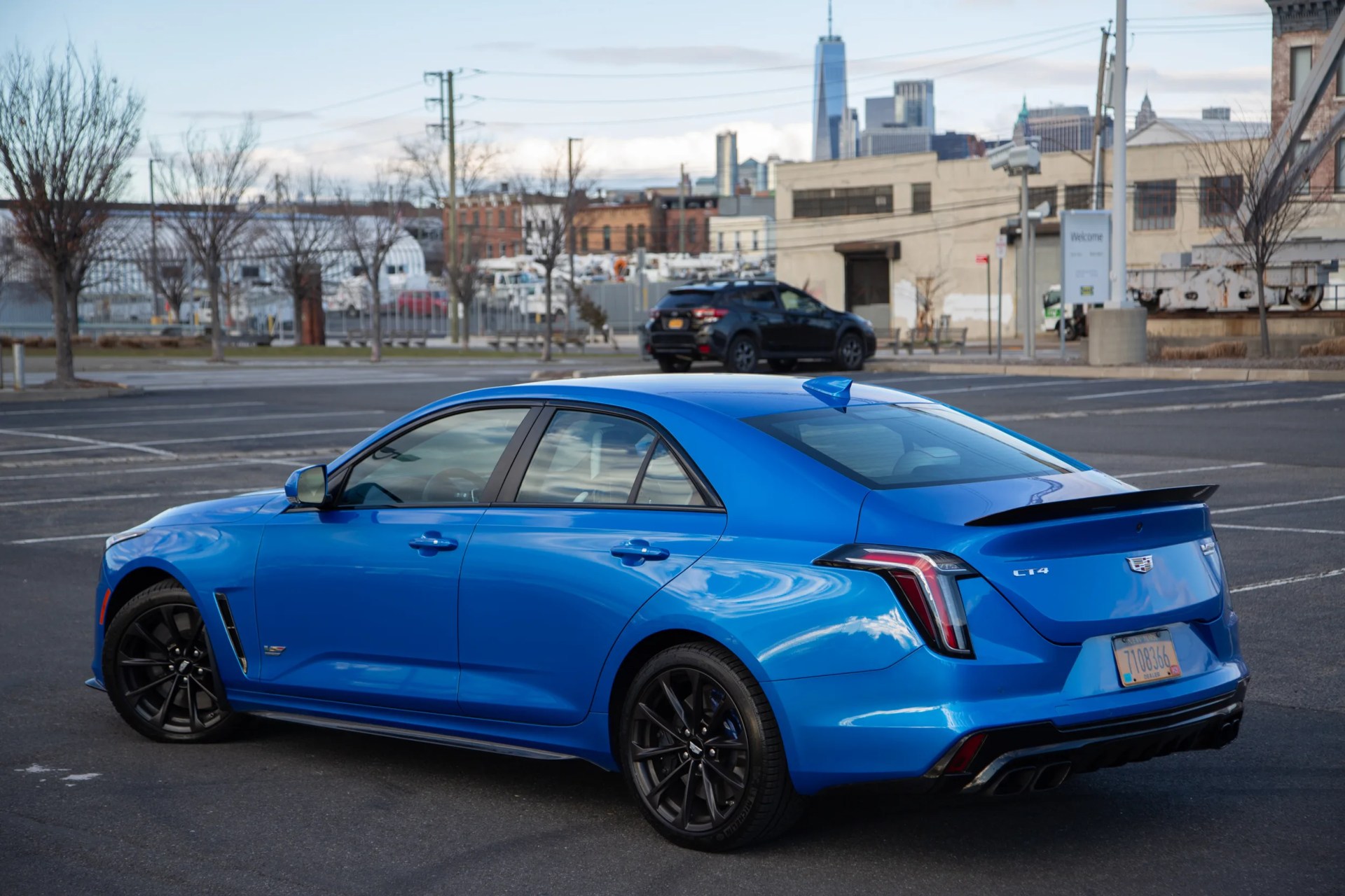 rear three quarter view of a blue cadillac ct4 v blackwing in a parking lot with brooklyn behind it