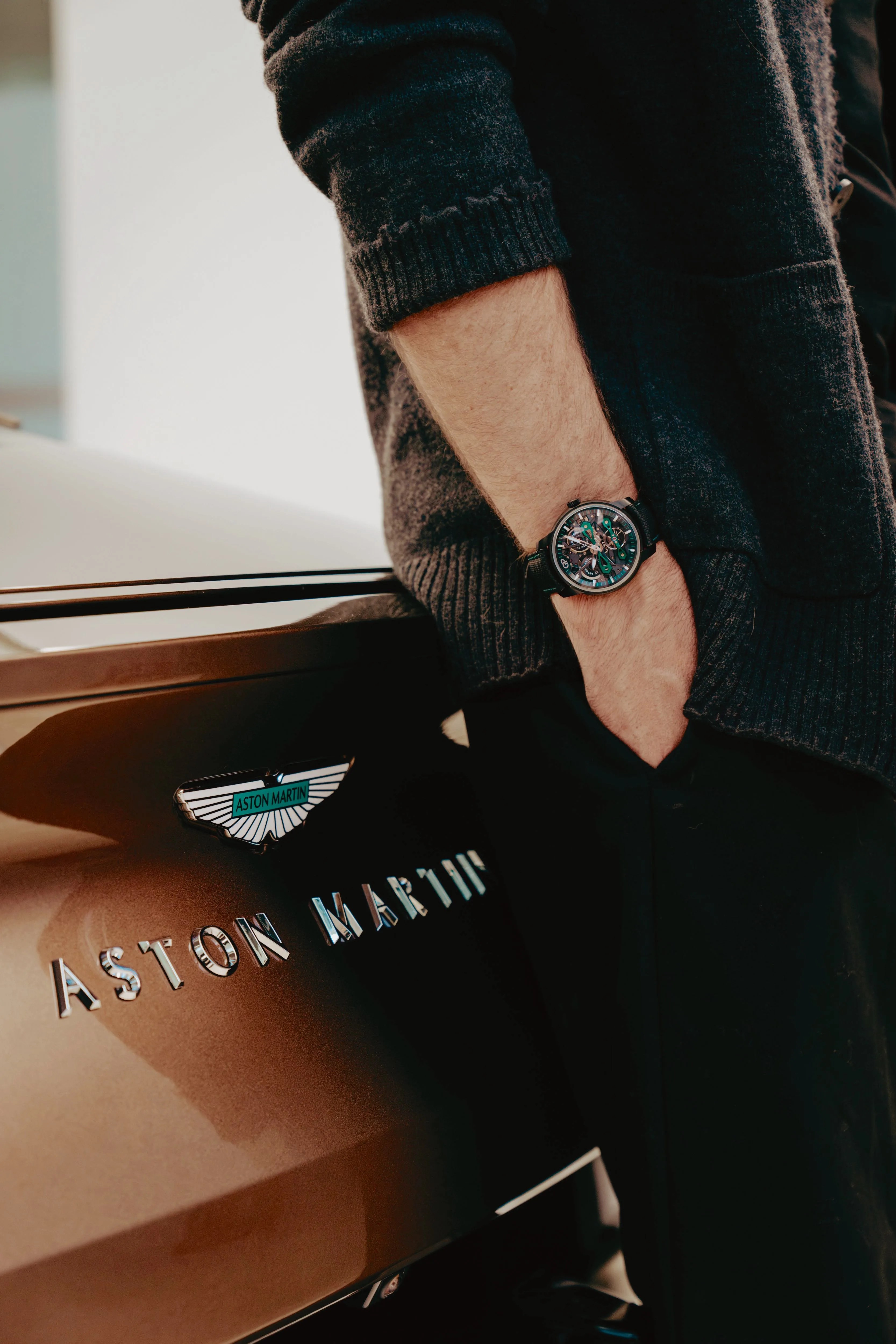 a man wears a Girard Perregaux watch next to an aston martin car