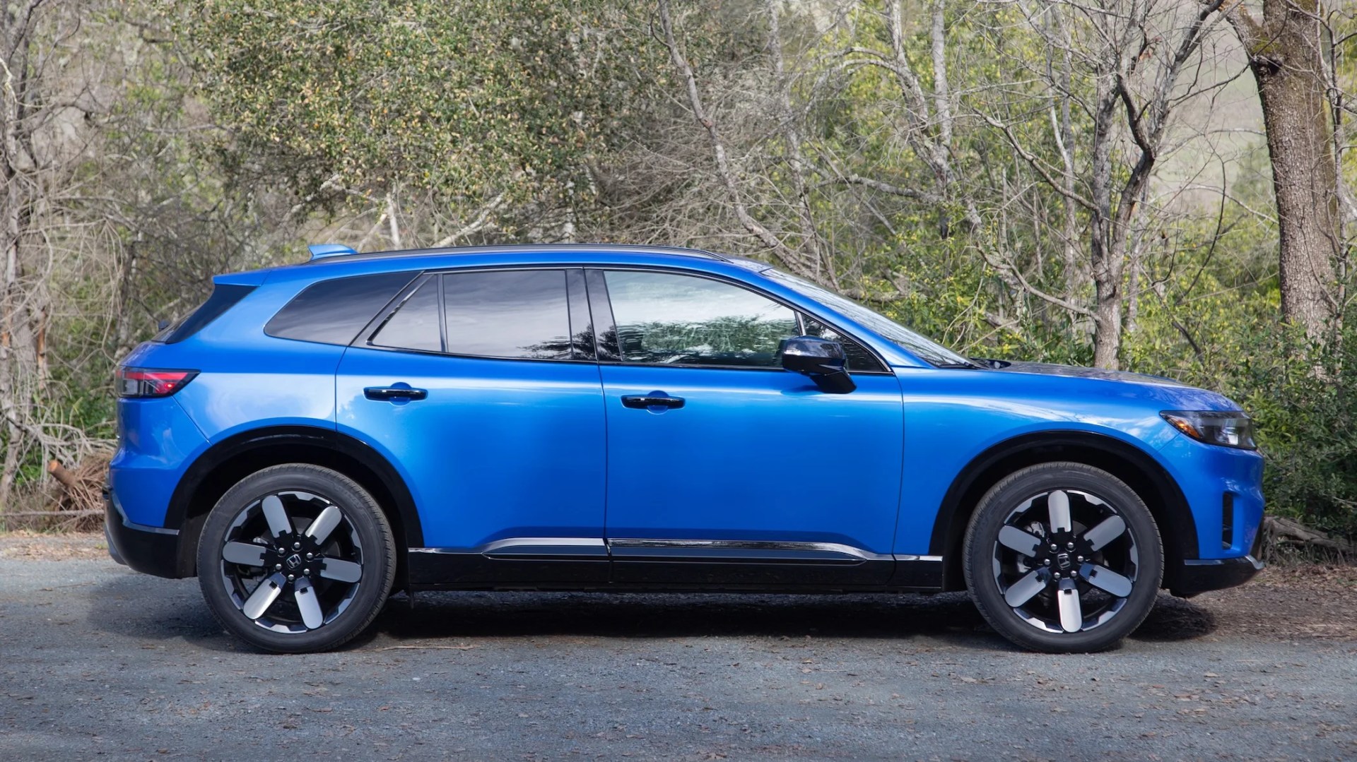 the side view of a blue 2024 honda prologue in front of some trees