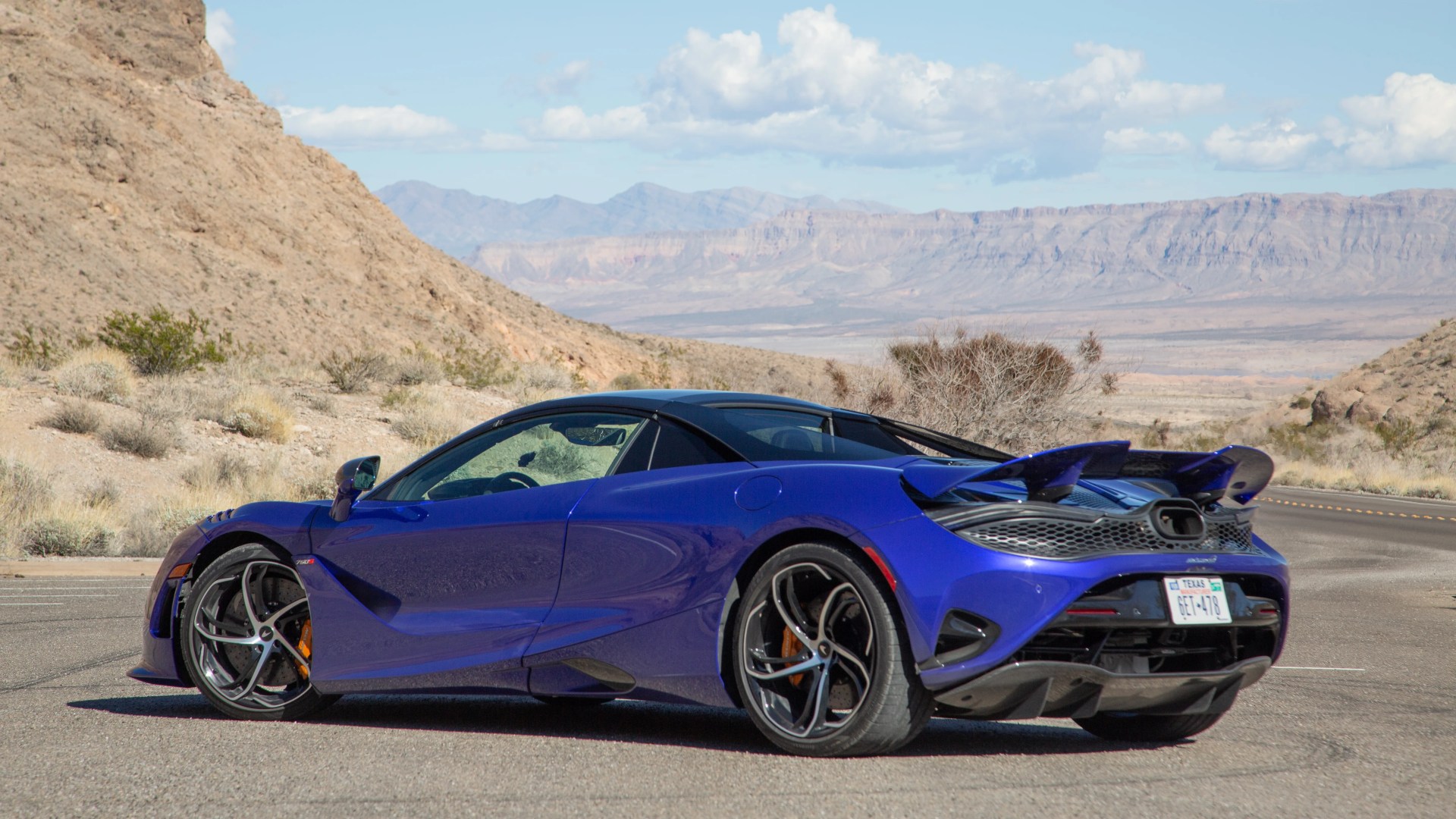 a purple blue mclaren 750s spider parked with mountains in the background