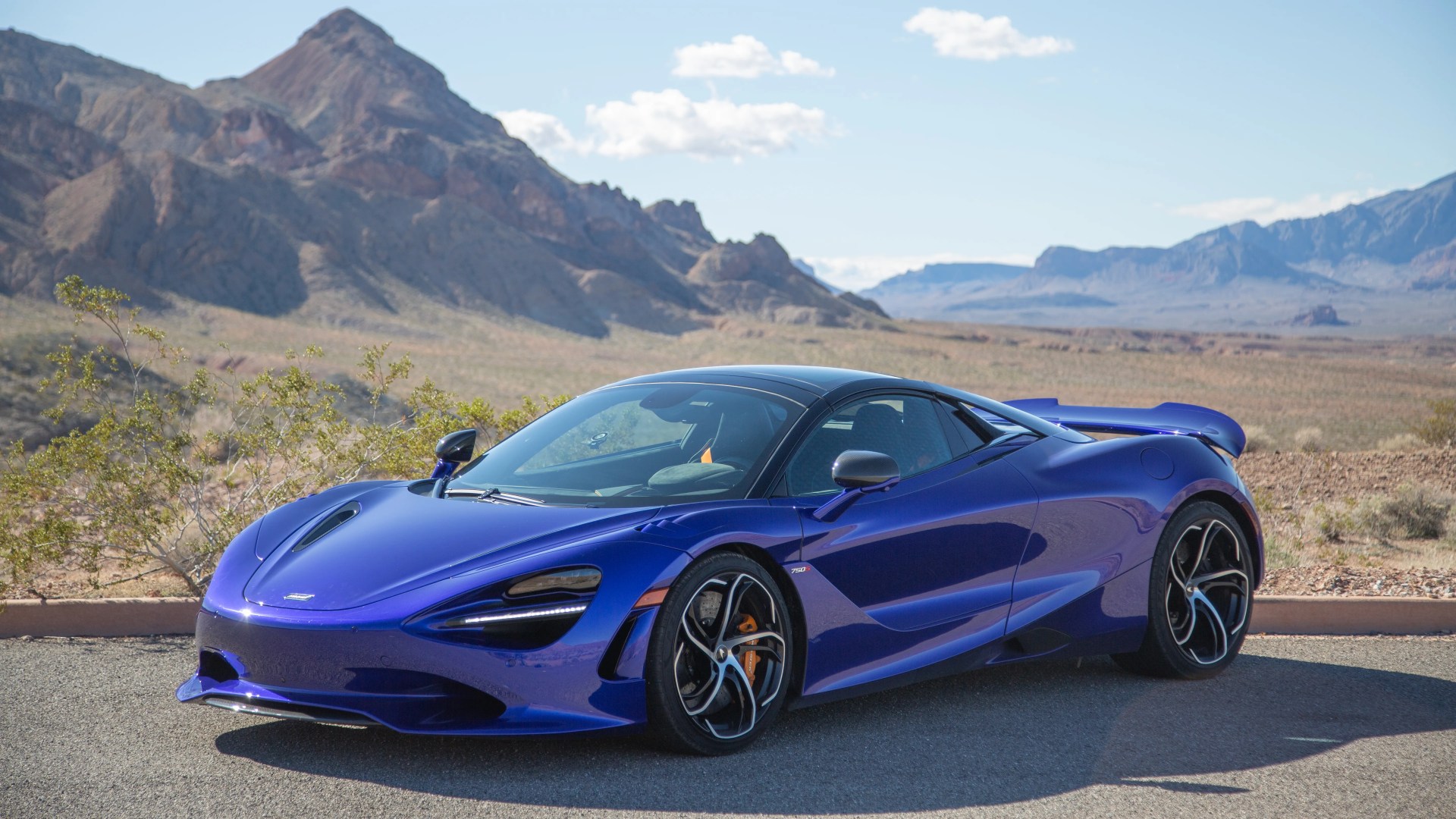 a purple blue mclaren 750s spider parked with mountains in the background