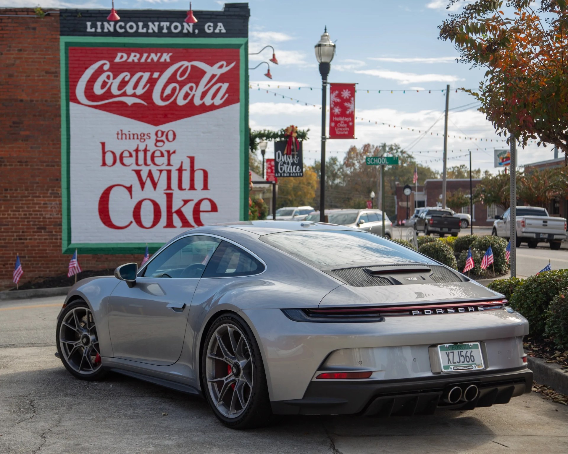 a silver porsche 911 gt3 touring parked in front of a coca cola sign