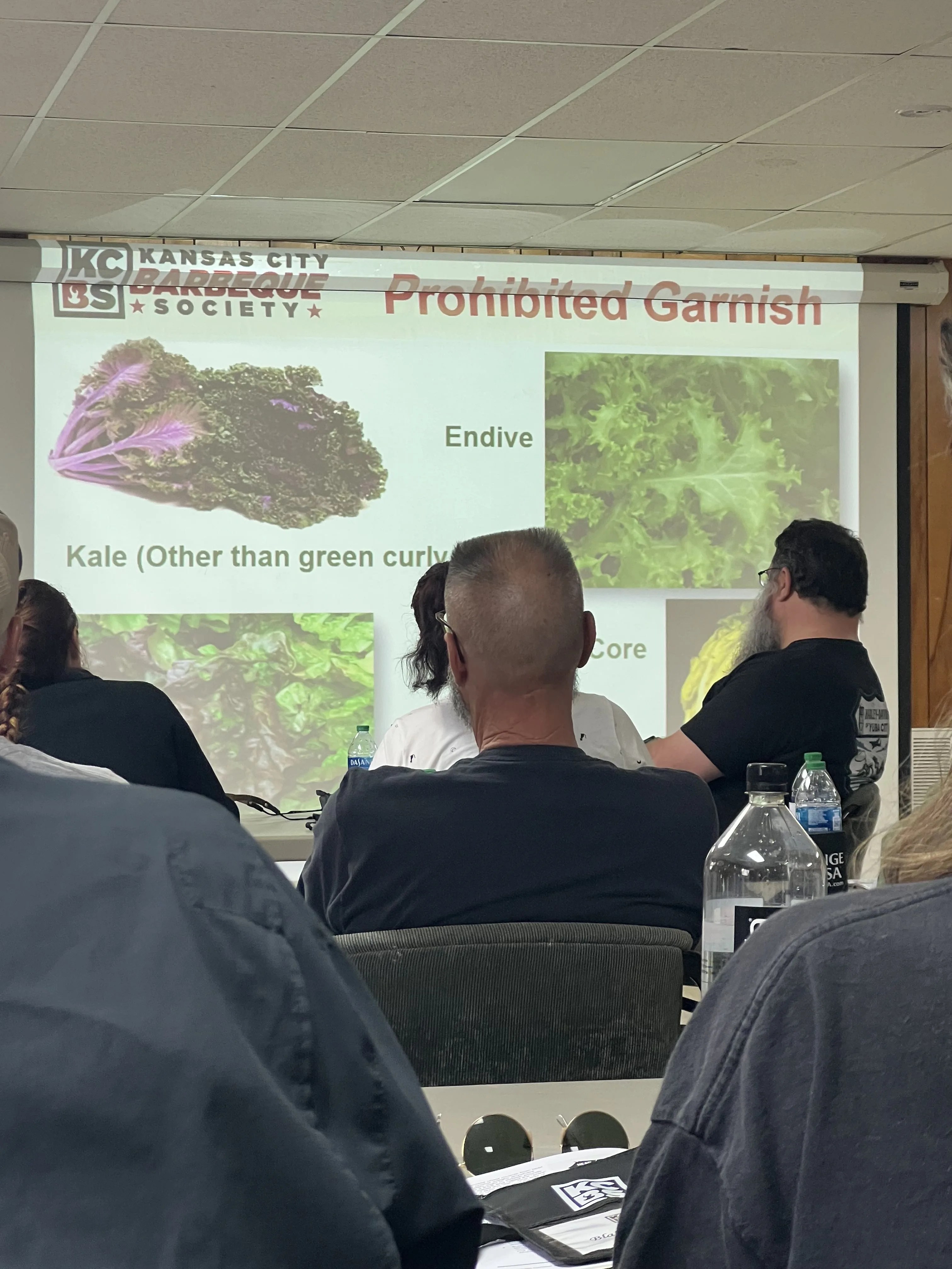 adults sit in a room looking at powerpoint presentation about garnishes