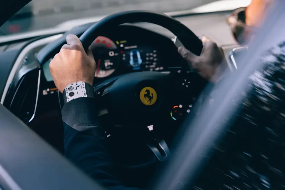 a driver wears a richard mille watch behind the wheel of a ferrari