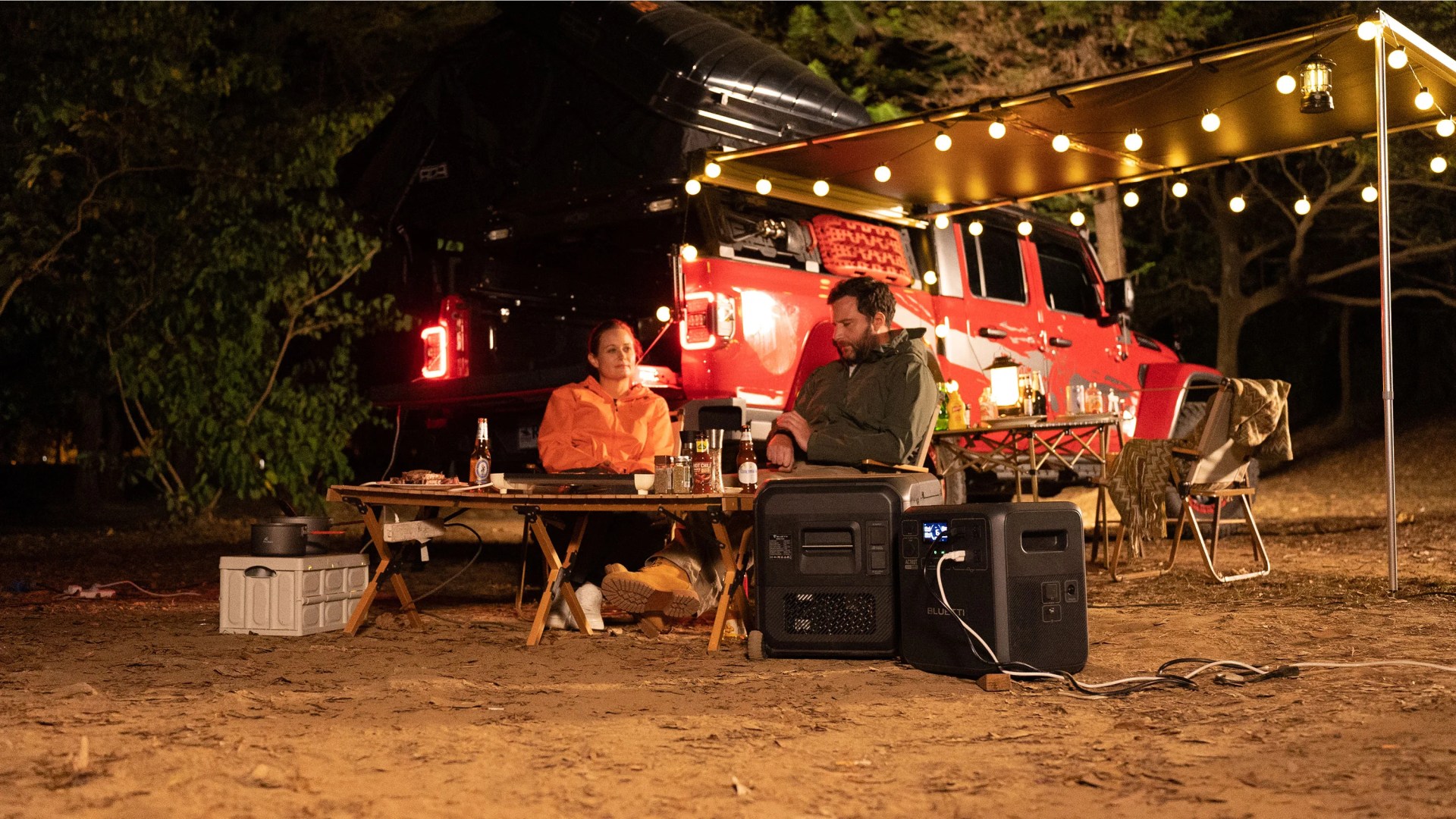 woman and man camping by trailer with fairy lights using Bluetti AC180T + Multicooler