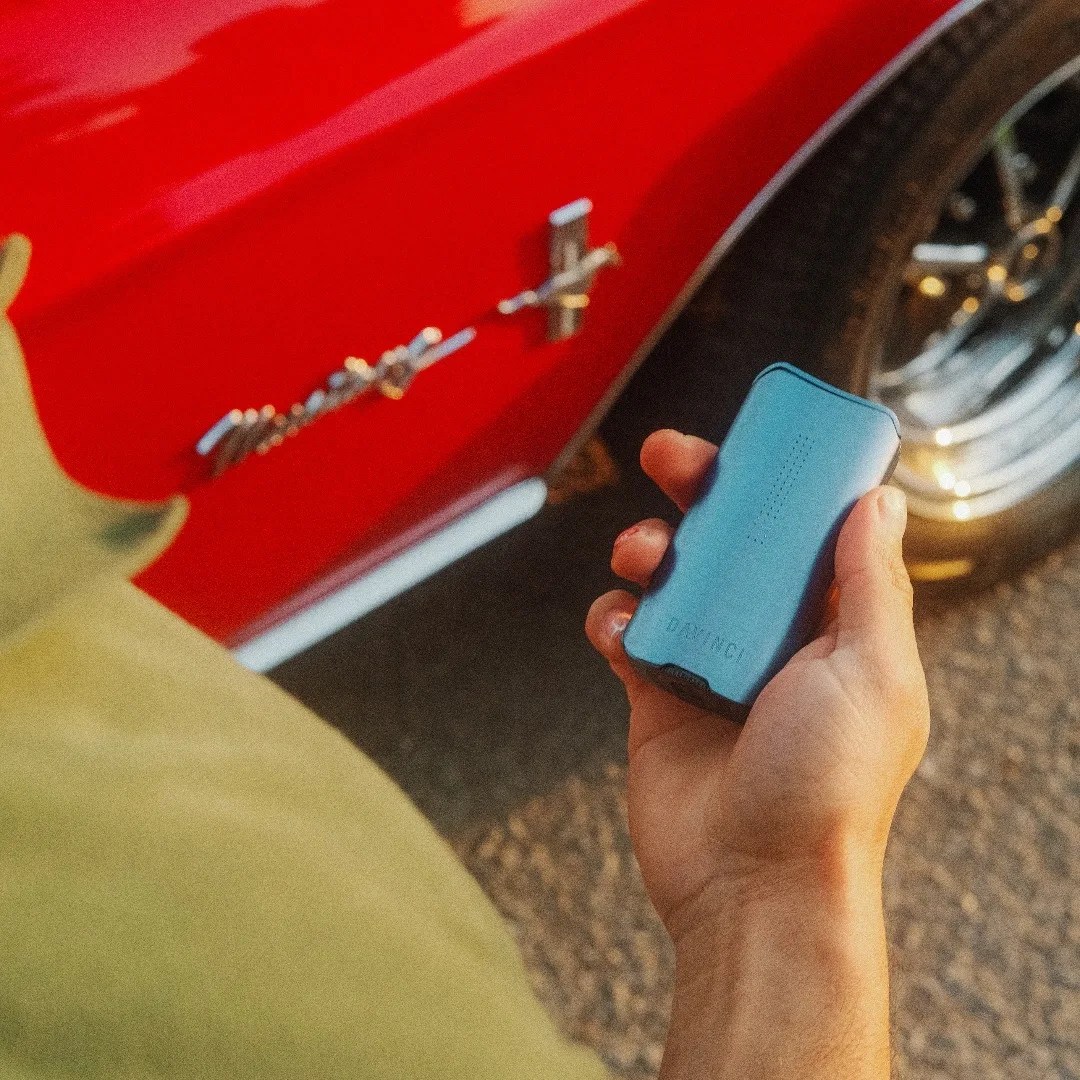 A hand holding a DaVinci weed vaporizer in front of a Mustang car