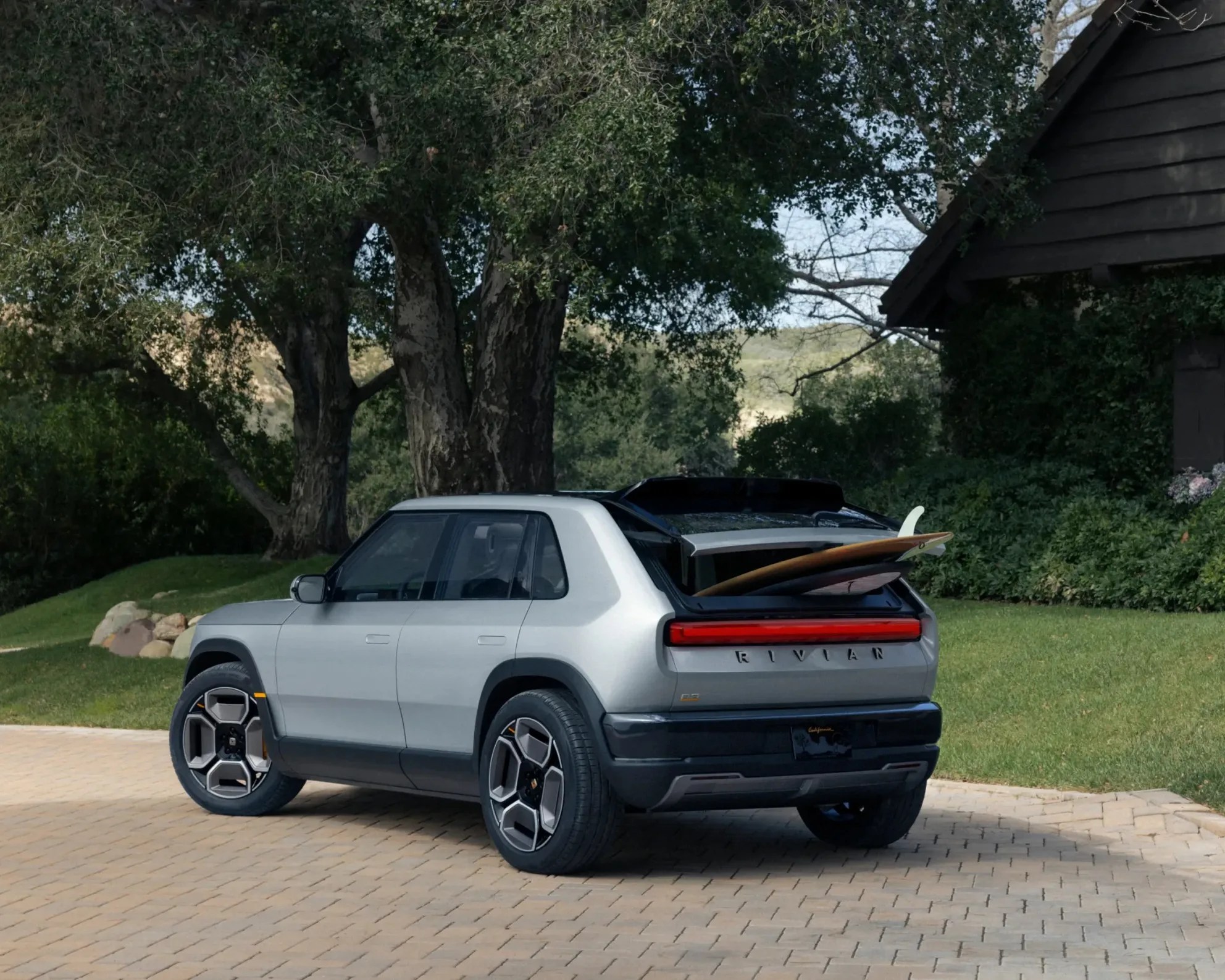 Rivian R3 in a driveway with a surfboard in the back