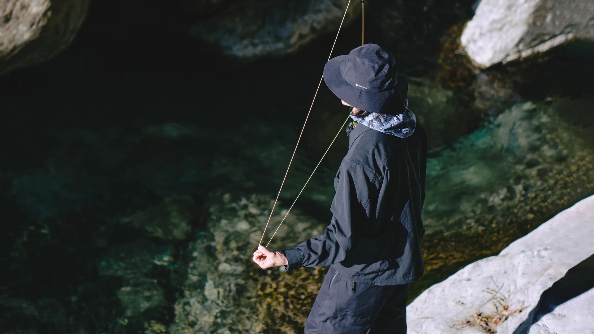a man fly fishing off a cliff rock wearing snow peak goretex outerwear