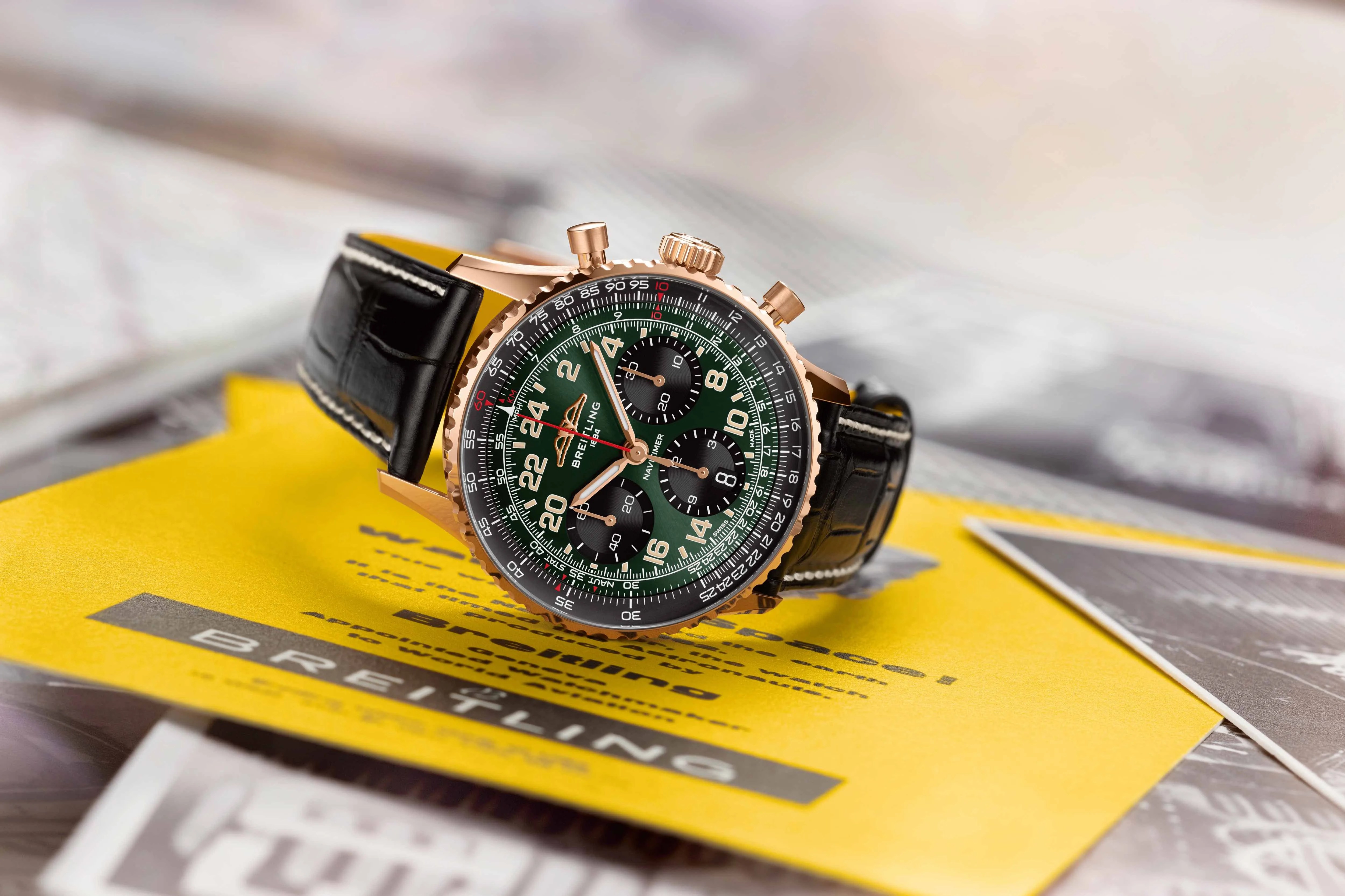 gold and green breitling watch on a yellow folder