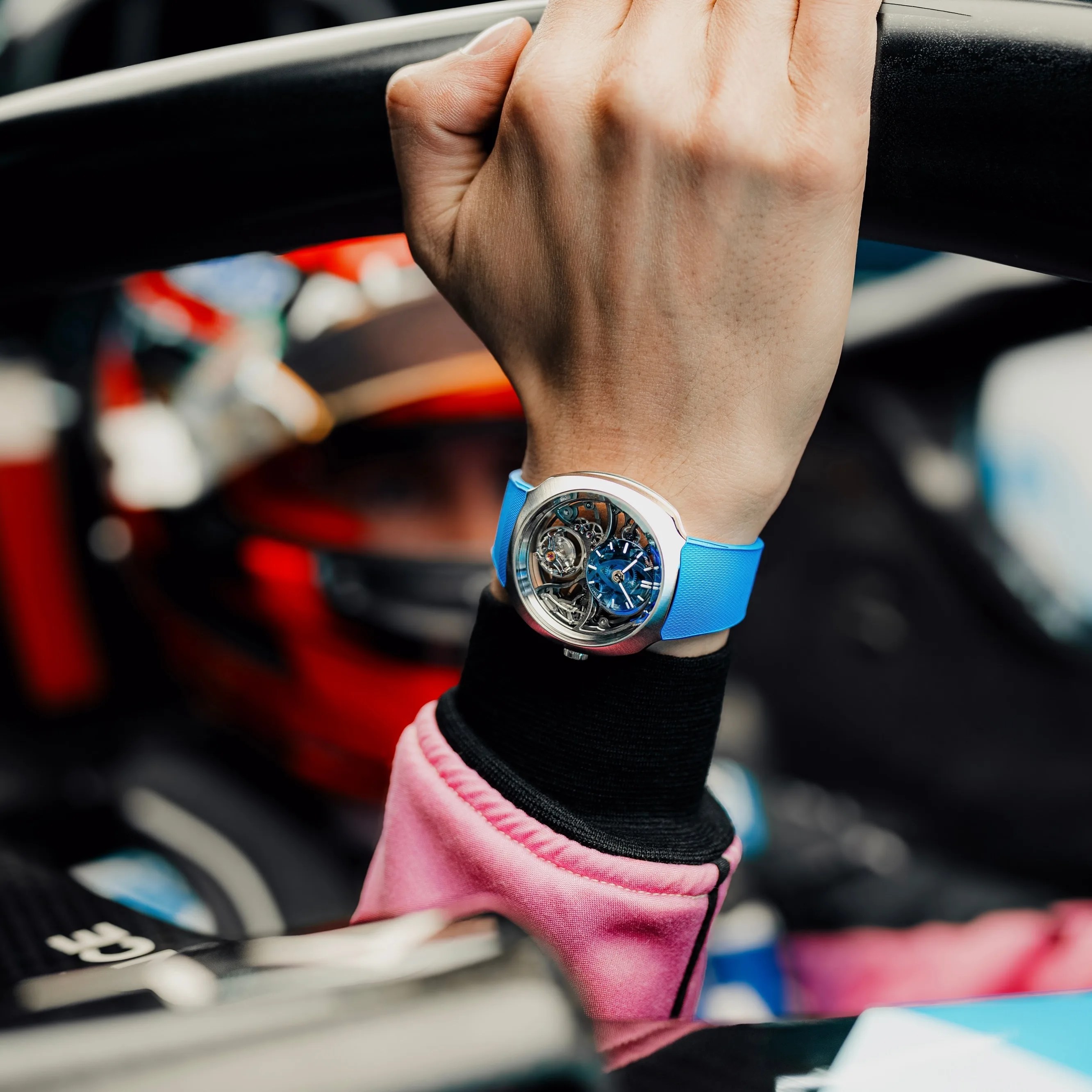 a team alpine driver poses in a race car wearing a moser watch