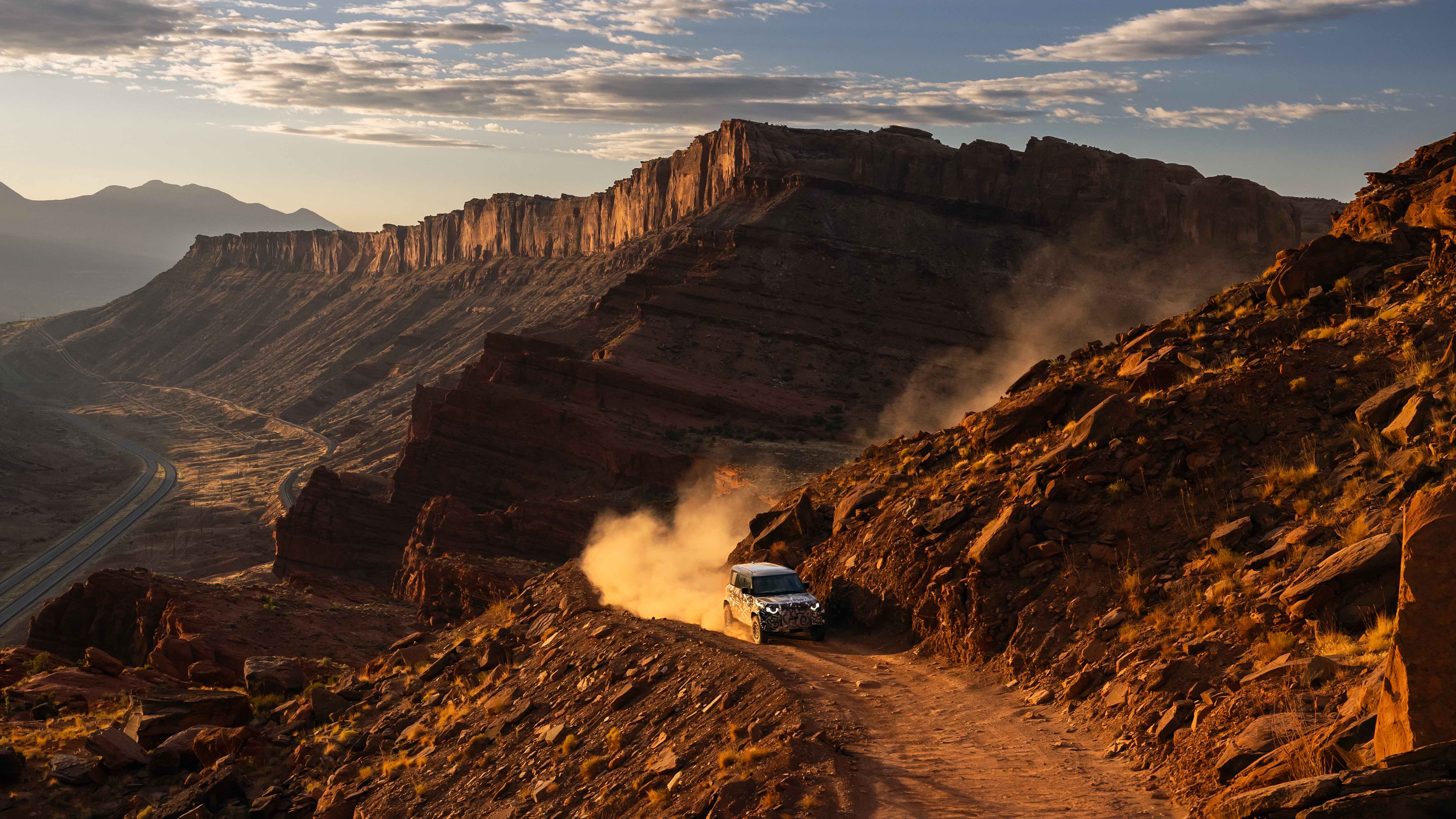 Camouflaged land rover defender suv drives on a dusty mountain trail