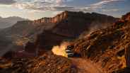 Camouflaged land rover defender suv drives on a dusty mountain trail