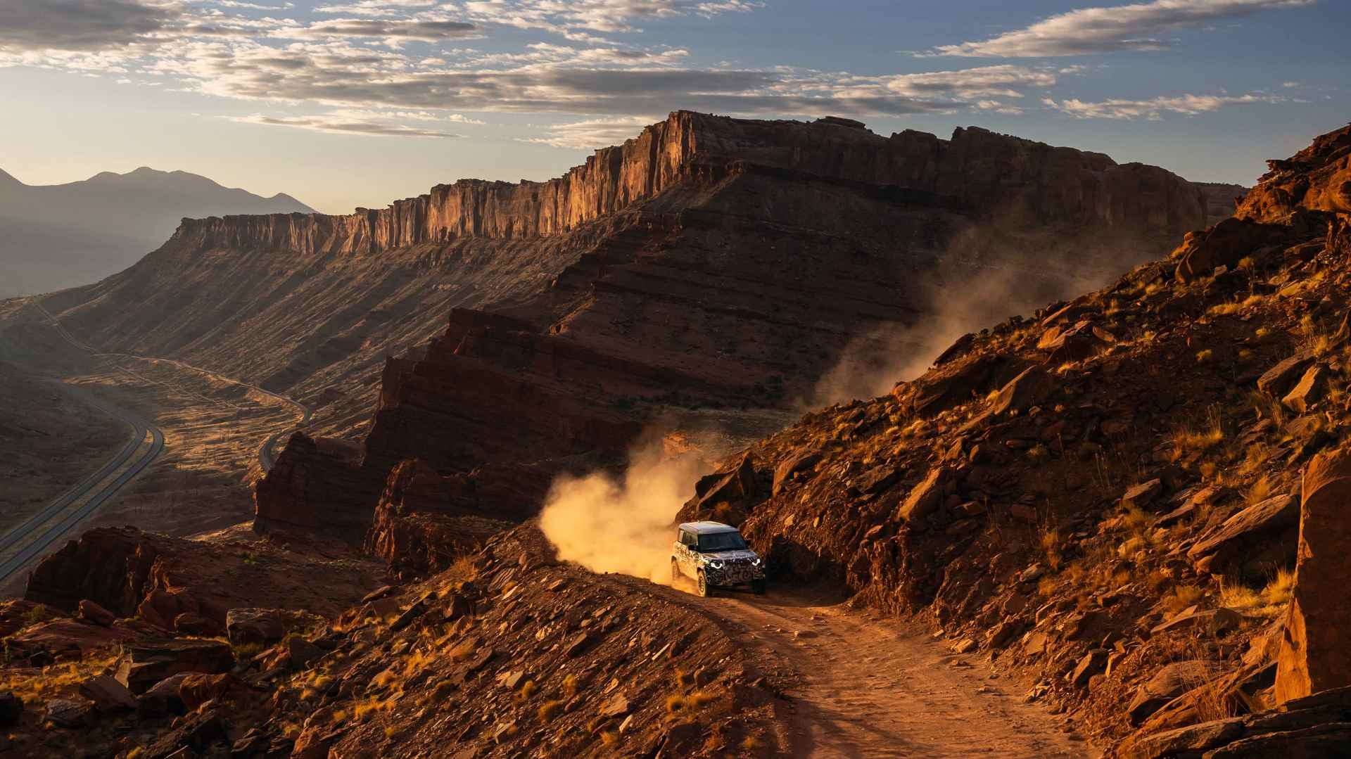 Camouflaged land rover defender suv drives on a dusty mountain trail