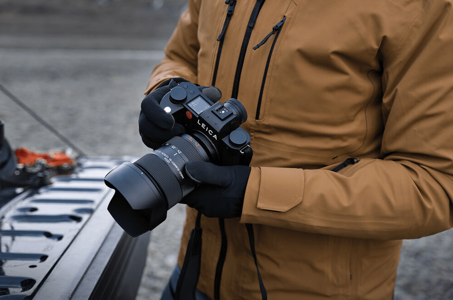 man in brown jacket and black gloves holds leica sl3 camera
