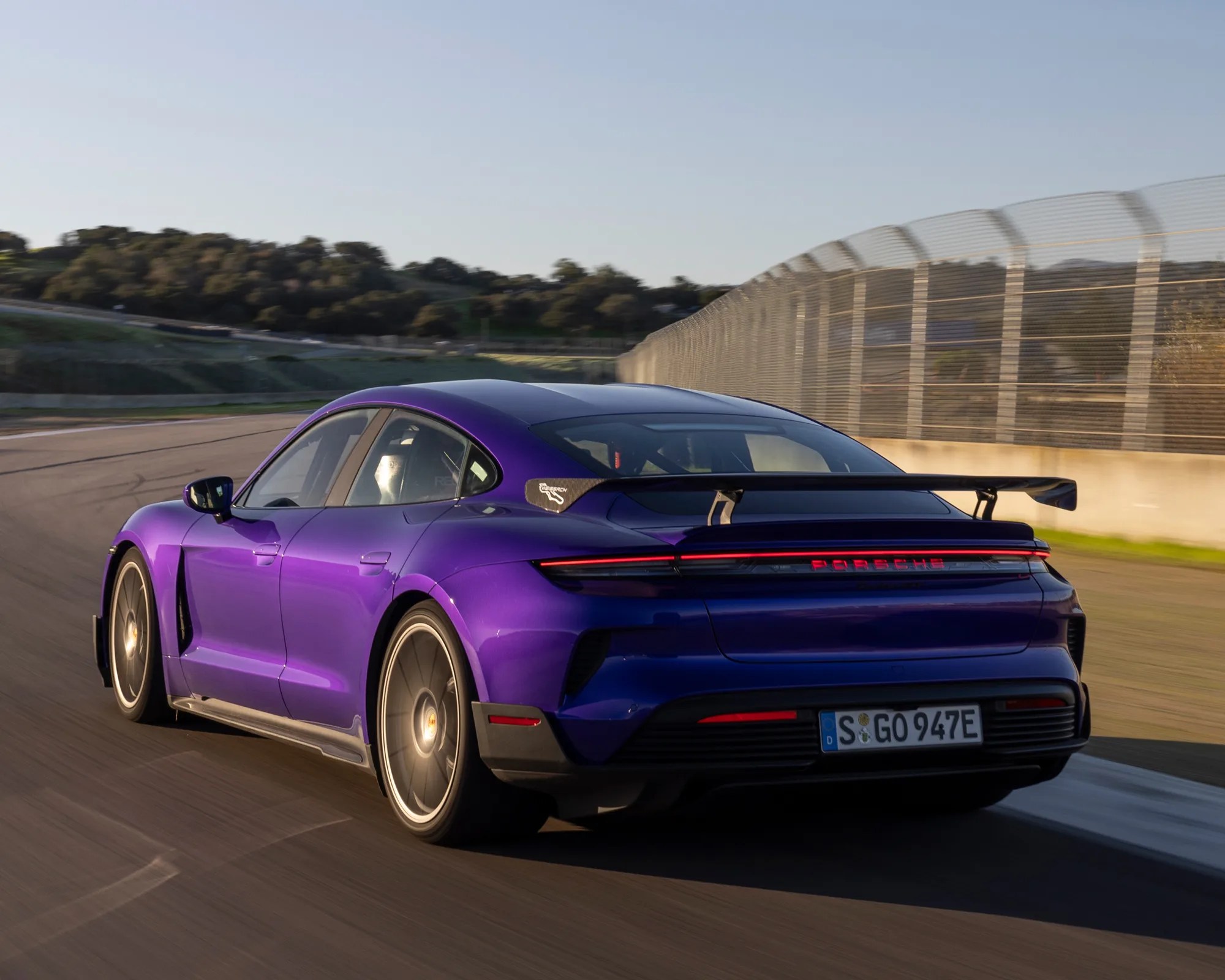 porsche taycan turbo gt in purple as seen from the rear three quarter angle while lapping a race track